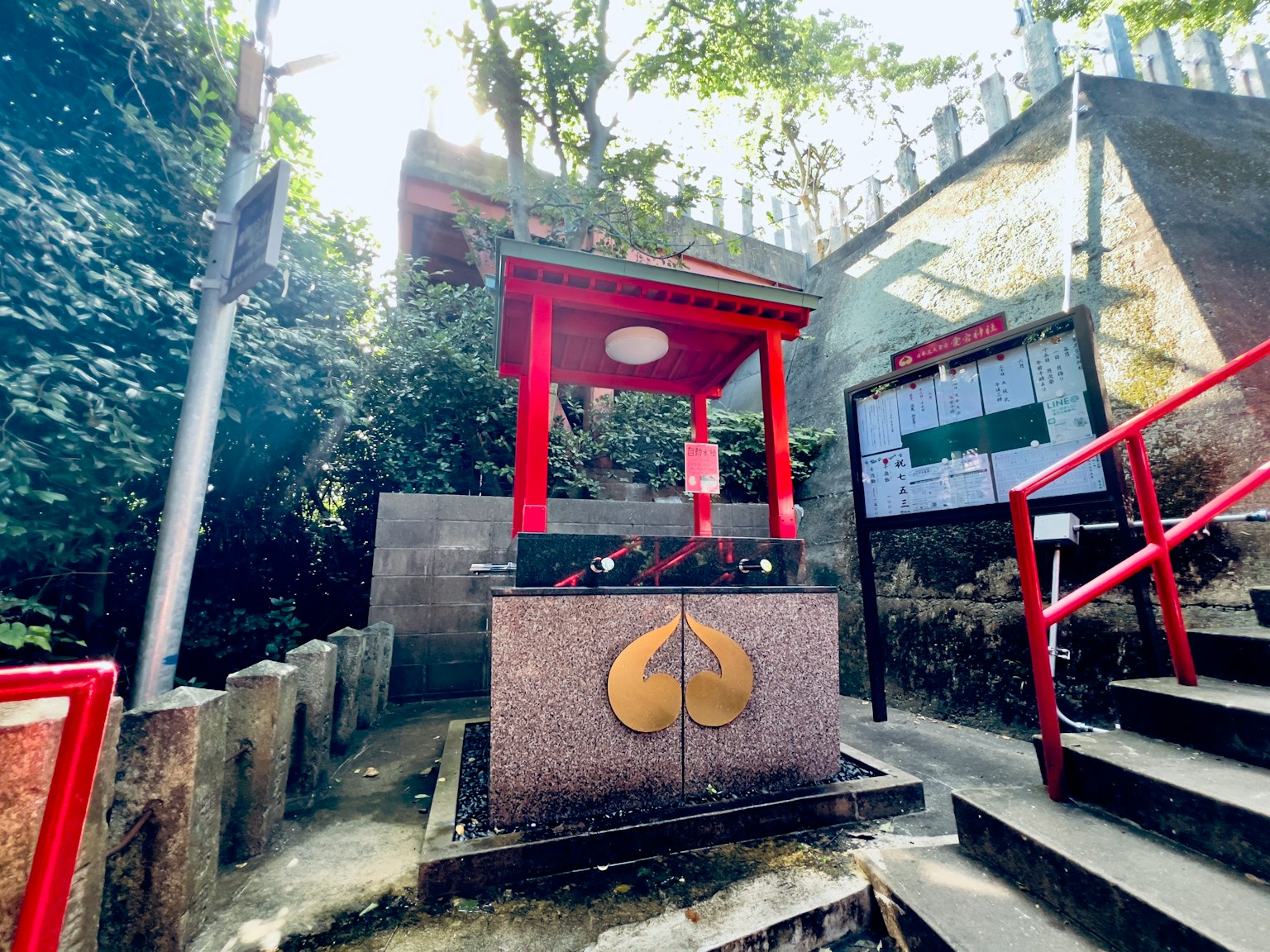 Rotes Torii am Wasser-Schrein umgeben von Grün und Treppen