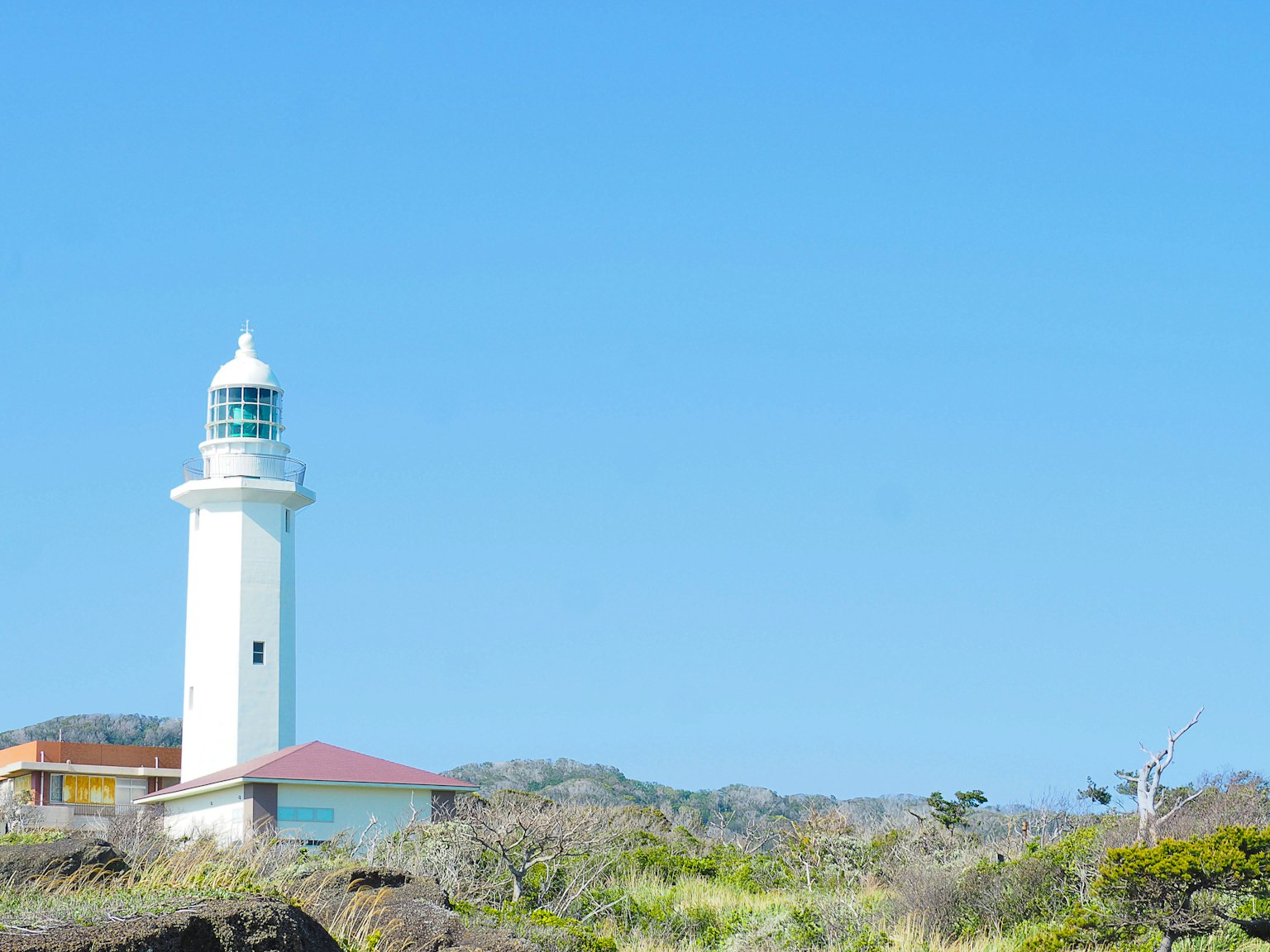 Un phare blanc sous un ciel bleu entouré d'un paysage verdoyant