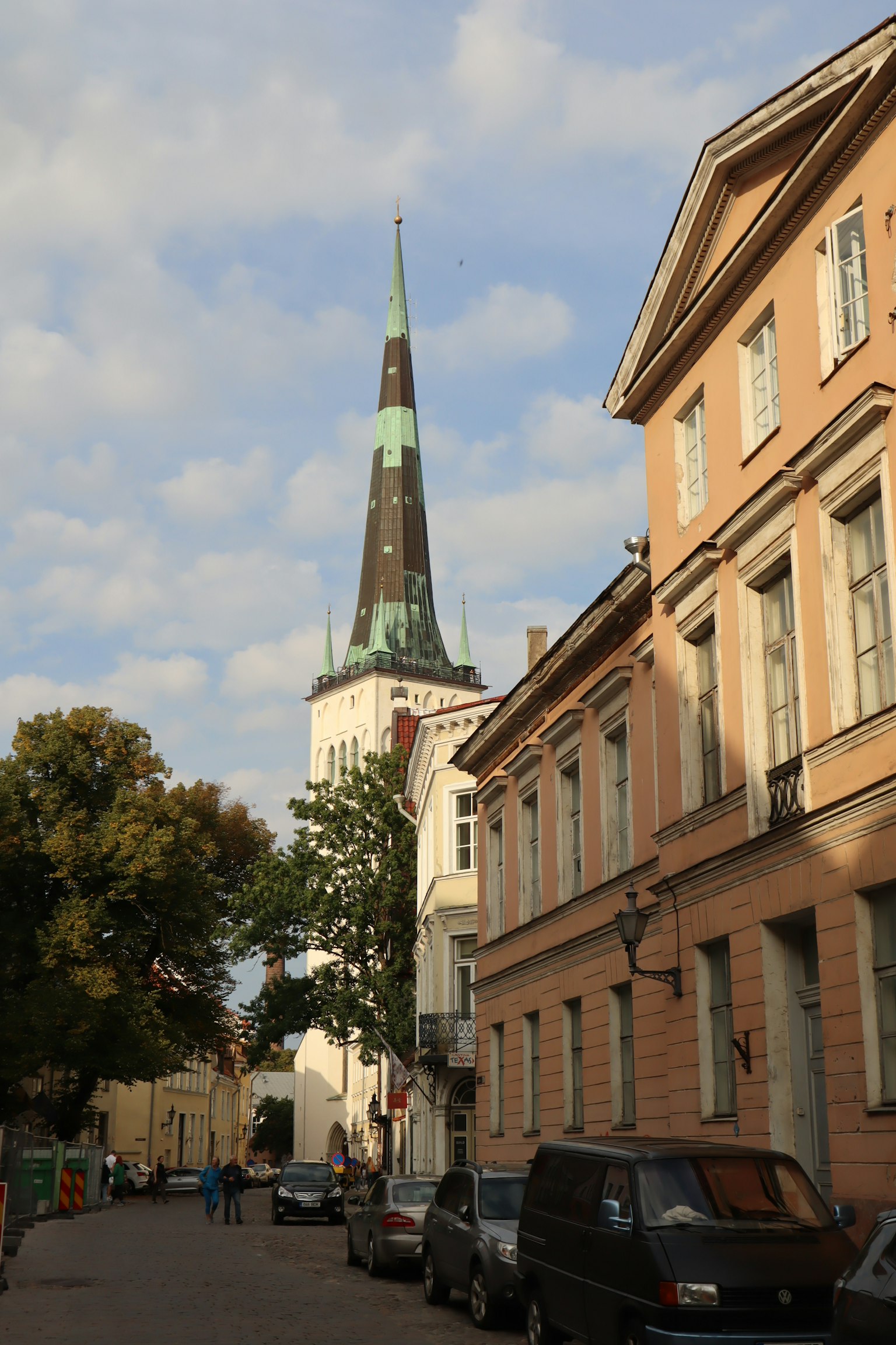 Vista de calle de Tallin Estonia con una torre de iglesia bajo un cielo azul con nubes