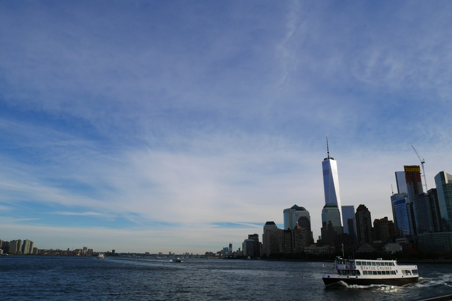 Skyline von New York mit dem One World Trade Center vor blauem Himmel und Wasserblick