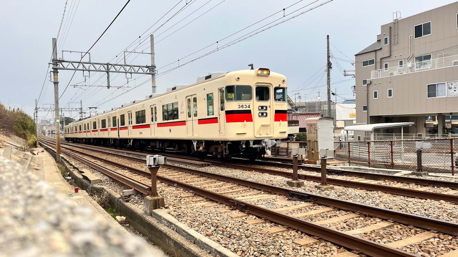 Un treno bianco che corre sui binari con edifici vicini e fili aerei