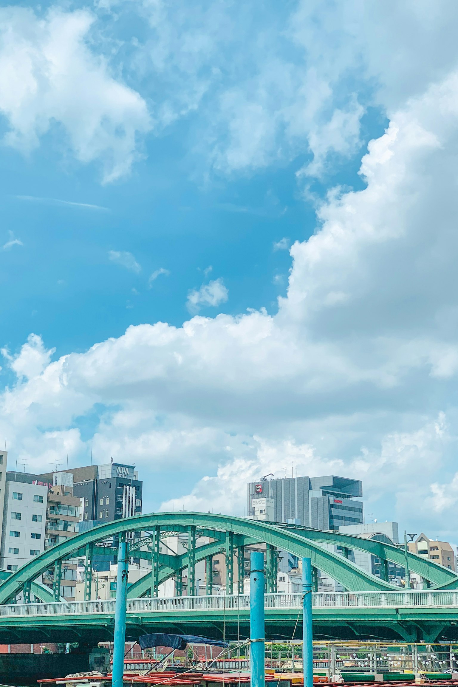 Green bridge under blue sky with white clouds and buildings