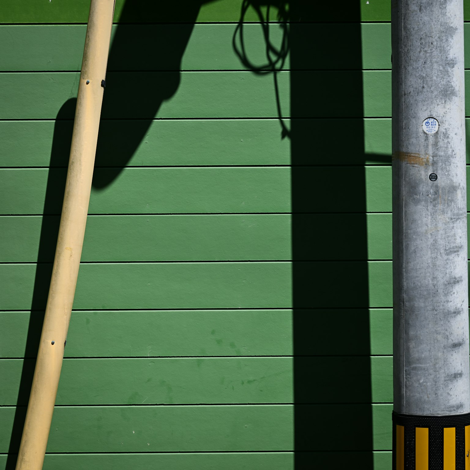Sombra de un poste de madera y un poste metálico contra una pared verde