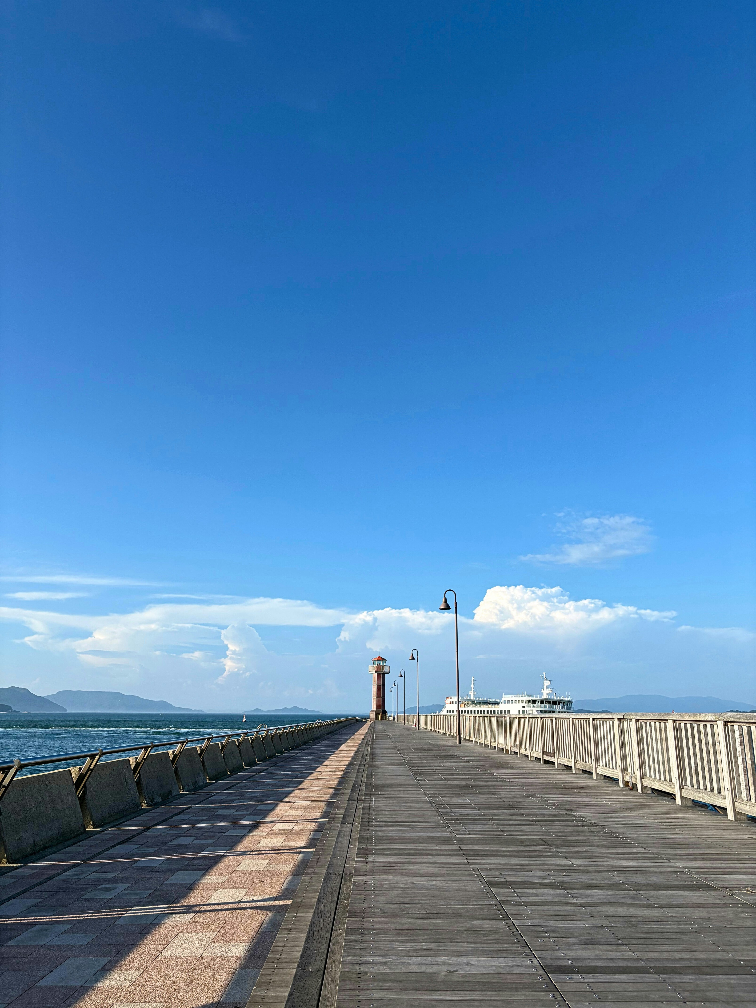 瀬戸内海を望む海沿いの遊歩道と青空の下の灯台