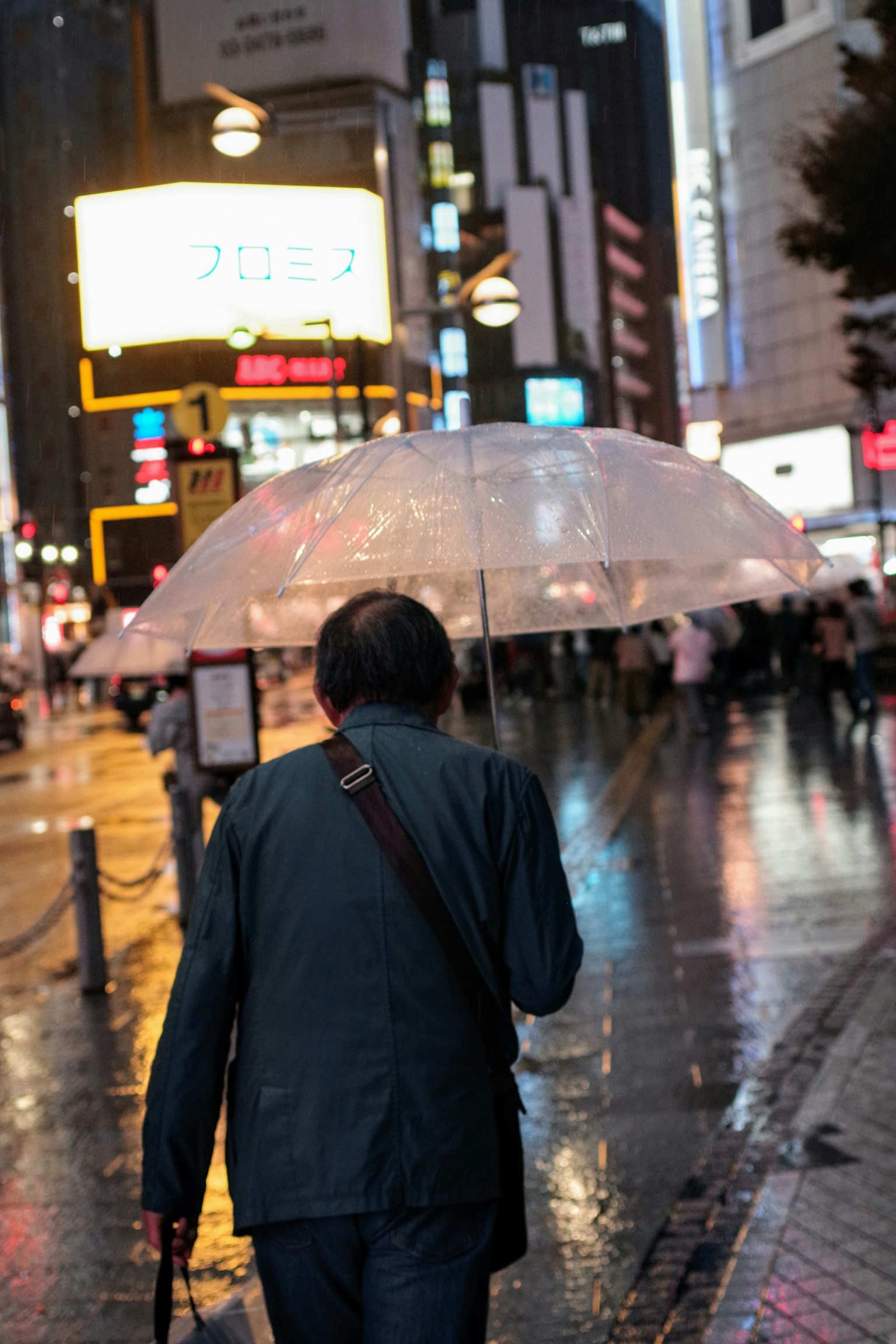 Un hombre caminando bajo la lluvia sosteniendo un paraguas transparente en un entorno urbano