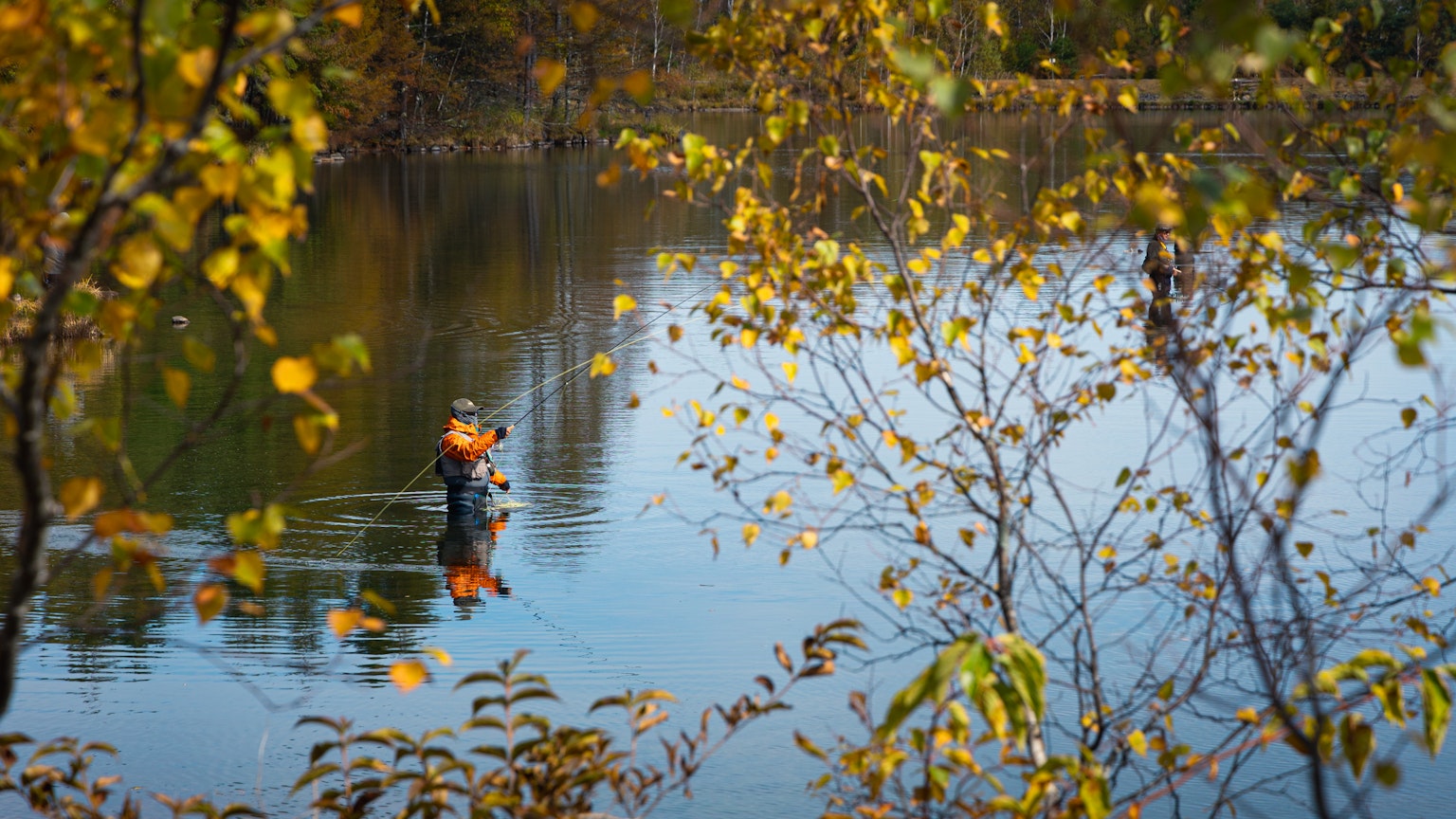 Silhouette di una persona che pesca su una superficie d'acqua con colori autunnali