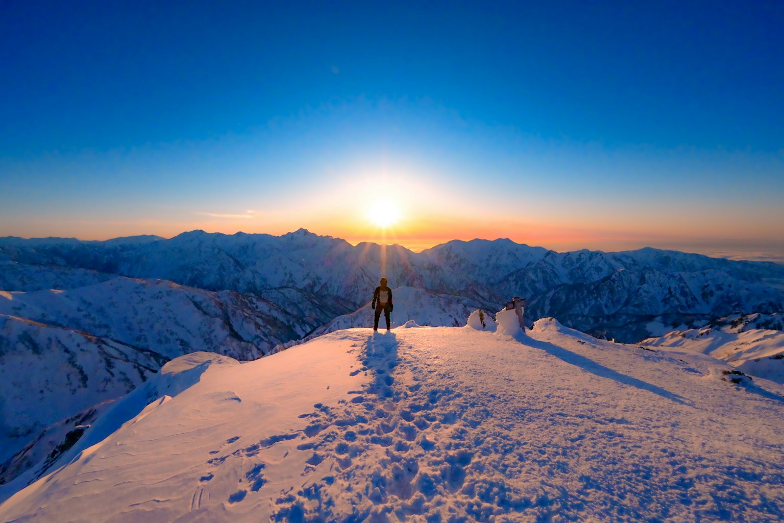 Silueta de un excursionista en la cima nevada de una montaña durante el amanecer