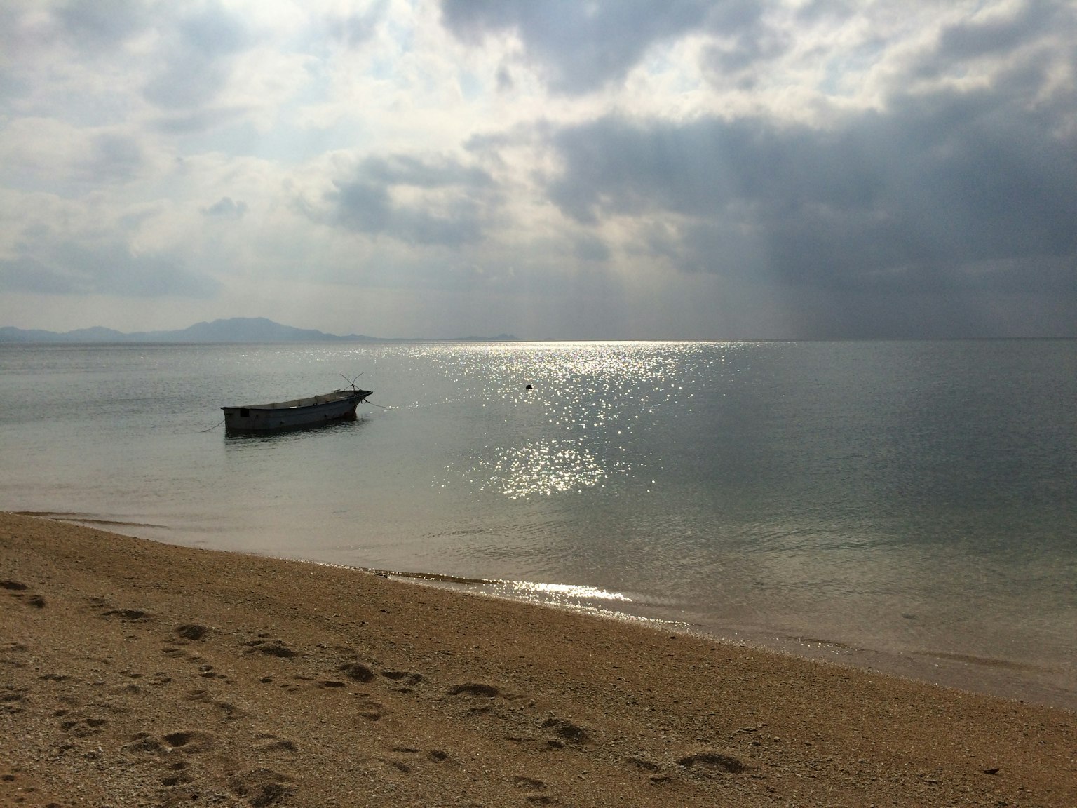 Una piccola barca che galleggia su un mare calmo con una spiaggia di sabbia