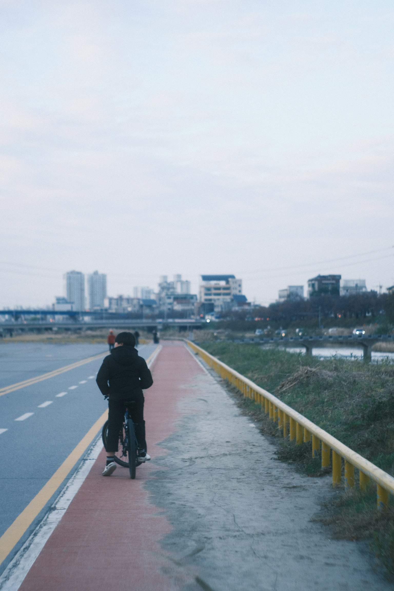 Eine Person fährt mit dem Fahrrad auf einem Weg am Fluss mit einer Stadtlandschaft im Hintergrund