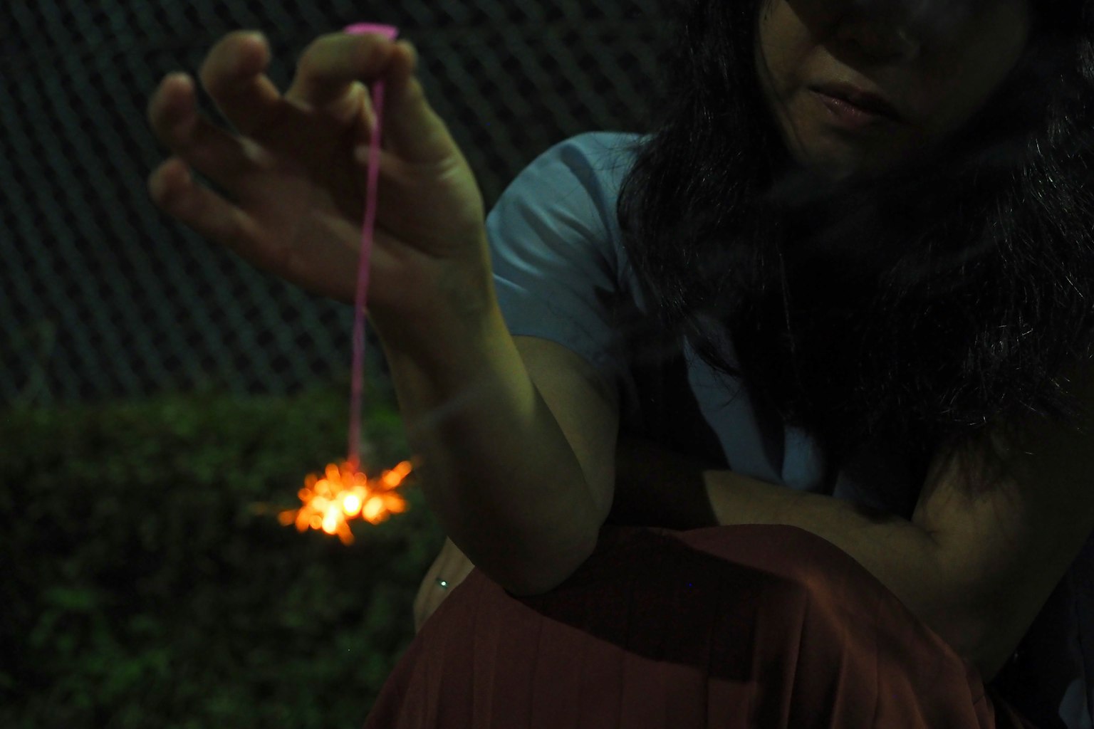 A woman holding a sparkler with bright sparks against a dark background