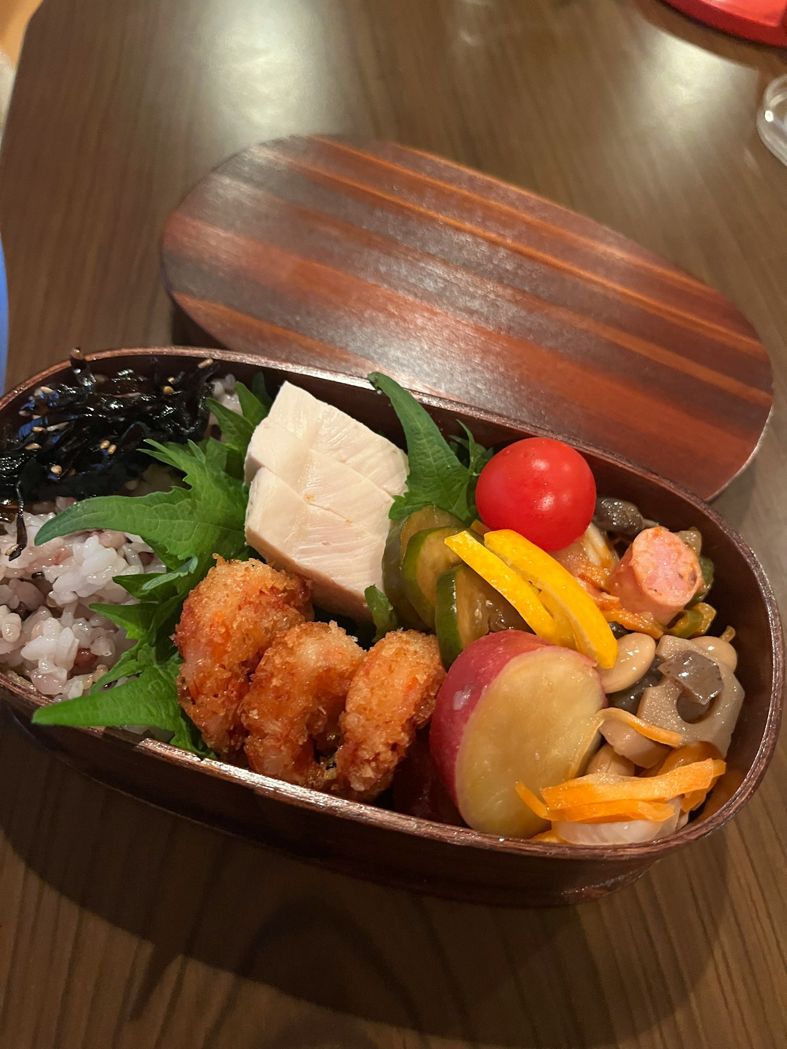精美的便当盒，内含炸虾、豆腐、樱桃番茄和时令蔬菜