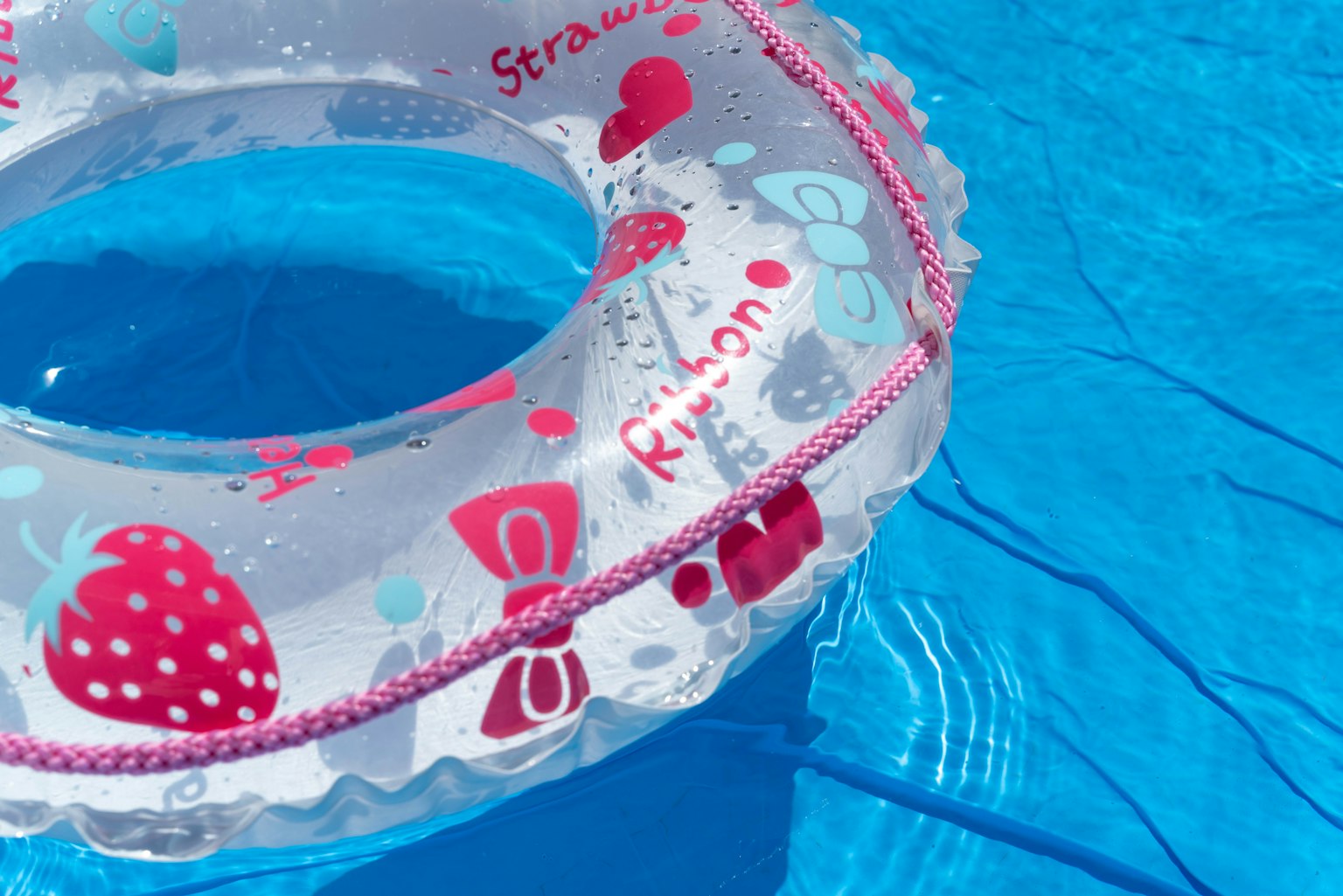 Strawberry-patterned inflatable ring floating on a blue pool