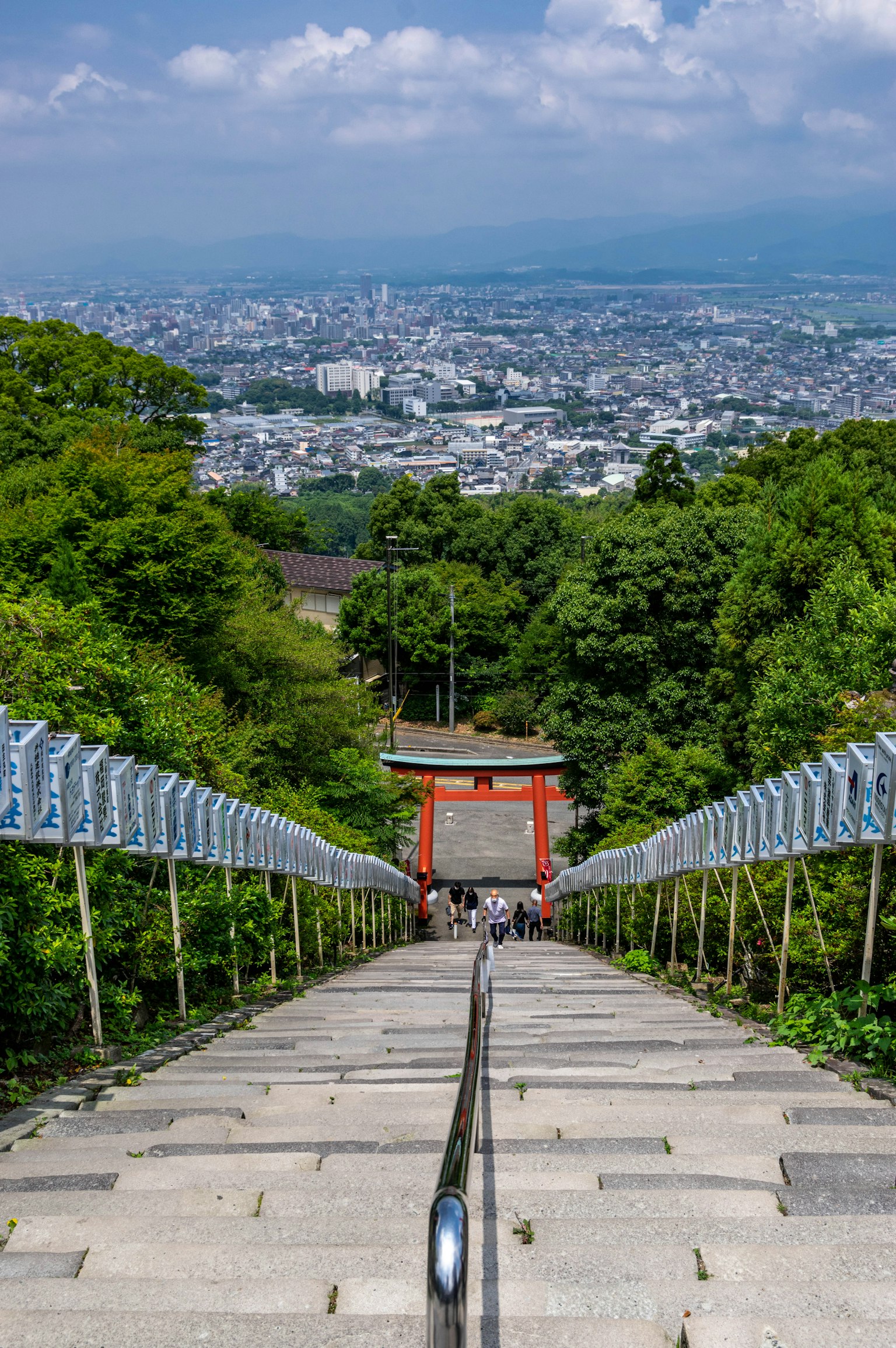 Una vista di una lunga scalinata circondata da vegetazione con un torii rosso visibile