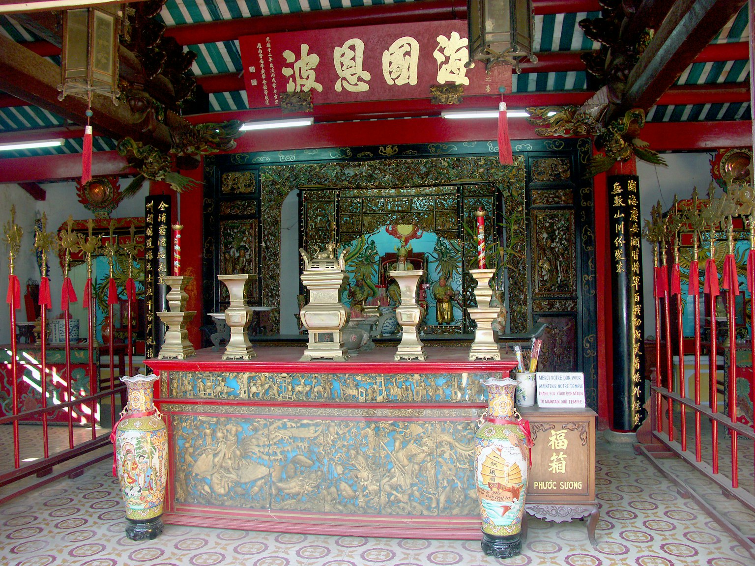 Interior of a beautifully decorated temple featuring red and gold colors with incense burners and ornaments on the altar