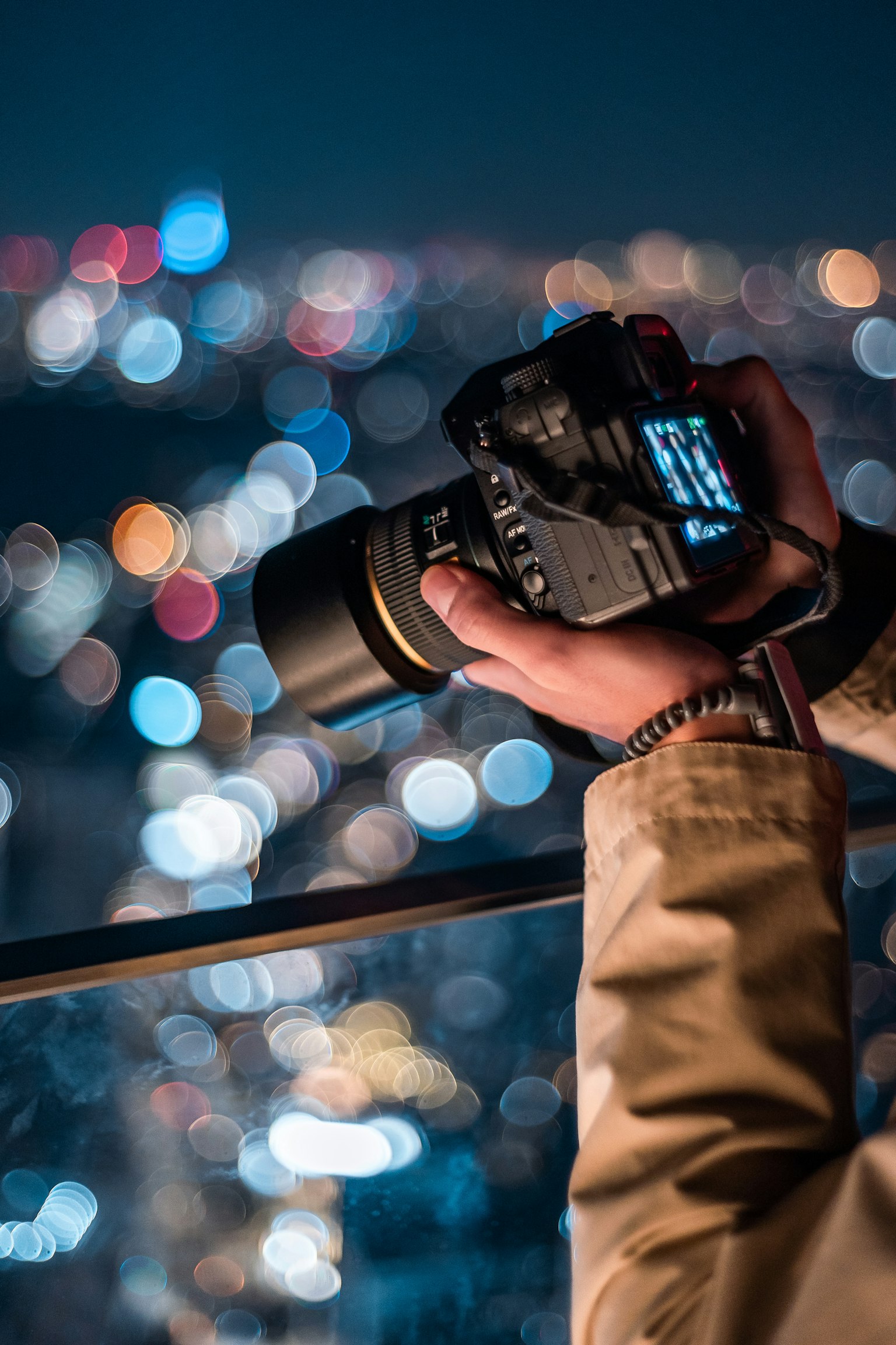 Hand eines Fotografen, der eine Kamera hält und nächtliche Stadtlichter aufnimmt