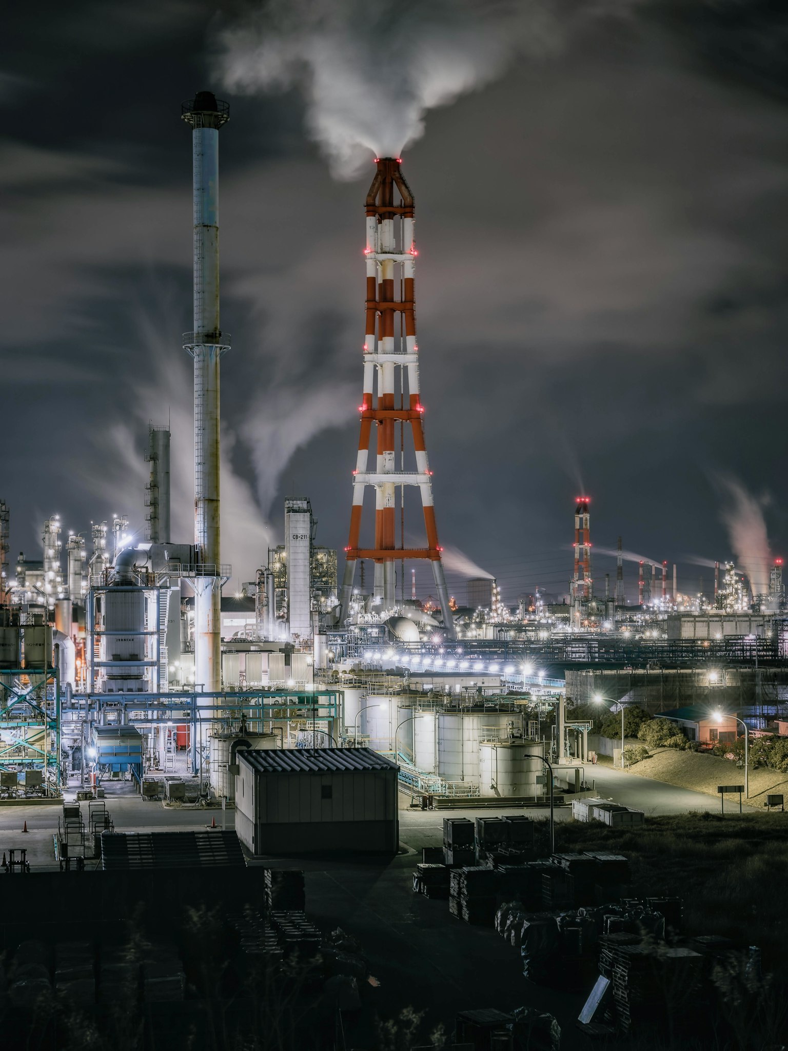 Red and white smokestack towering in an industrial area at night