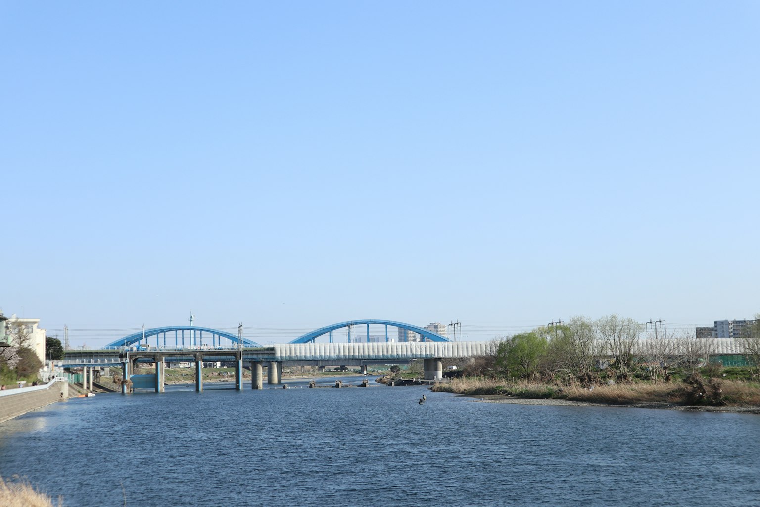 A blue bridge spanning a river under a clear sky