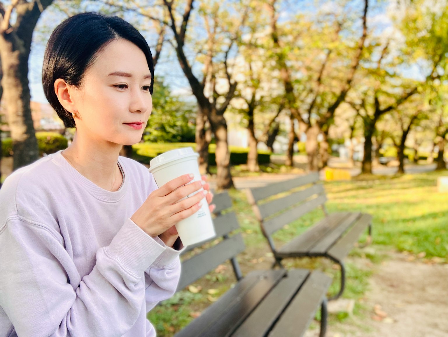 공원 벤치에 앉아 커피 컵을 들고 있는 여성