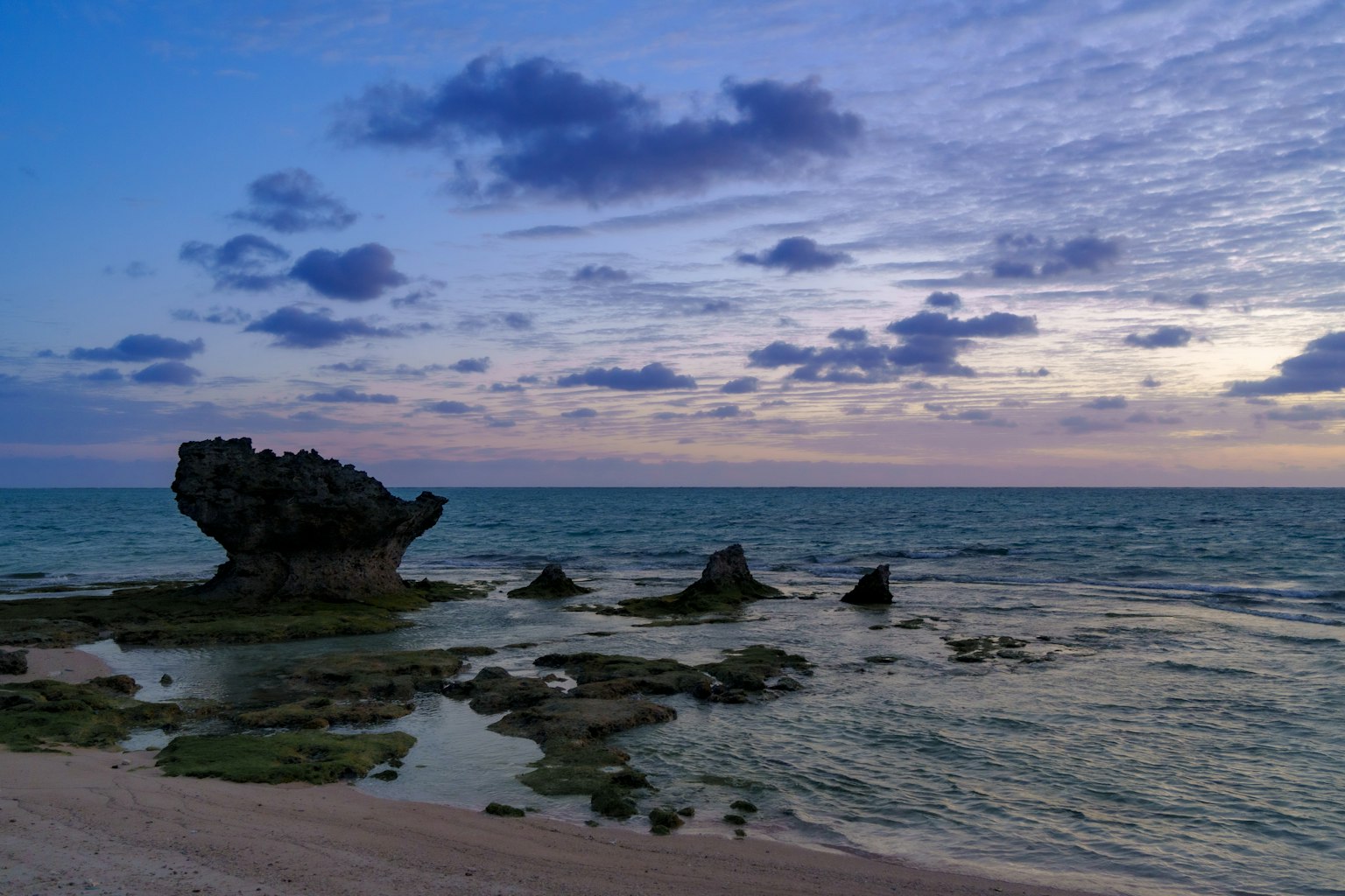 Coastal scene at dusk with a rock formation and calm sea