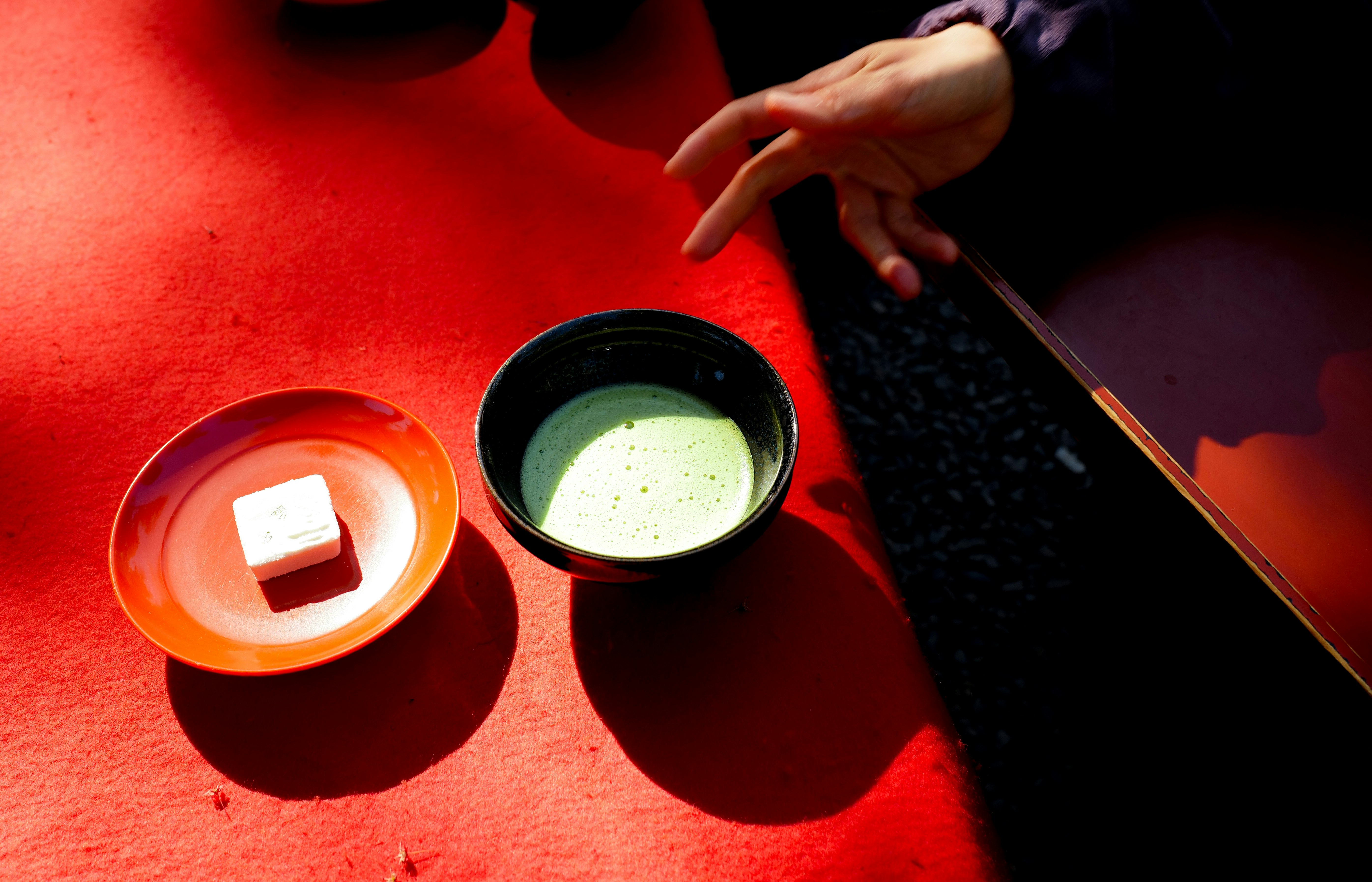 những chén nhỏ matcha có bọt và đồ ngọt dùng kèm trà trên bàn màu đỏ