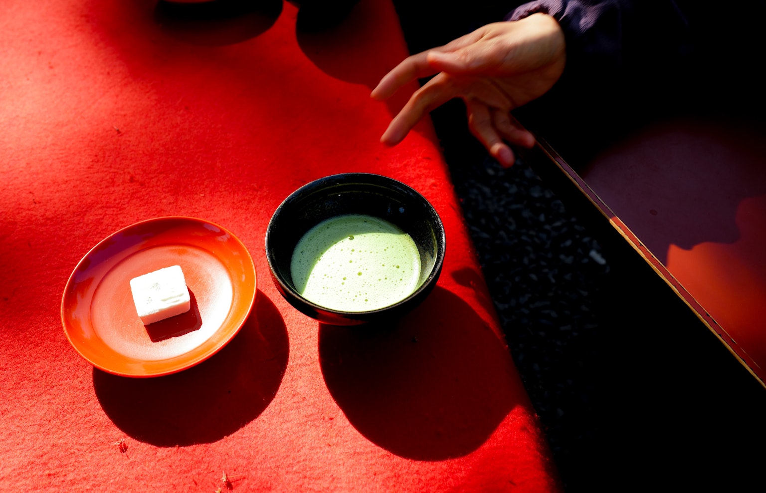 红色桌子上的抹茶碗和和果子盘子 一只手伸向抹茶