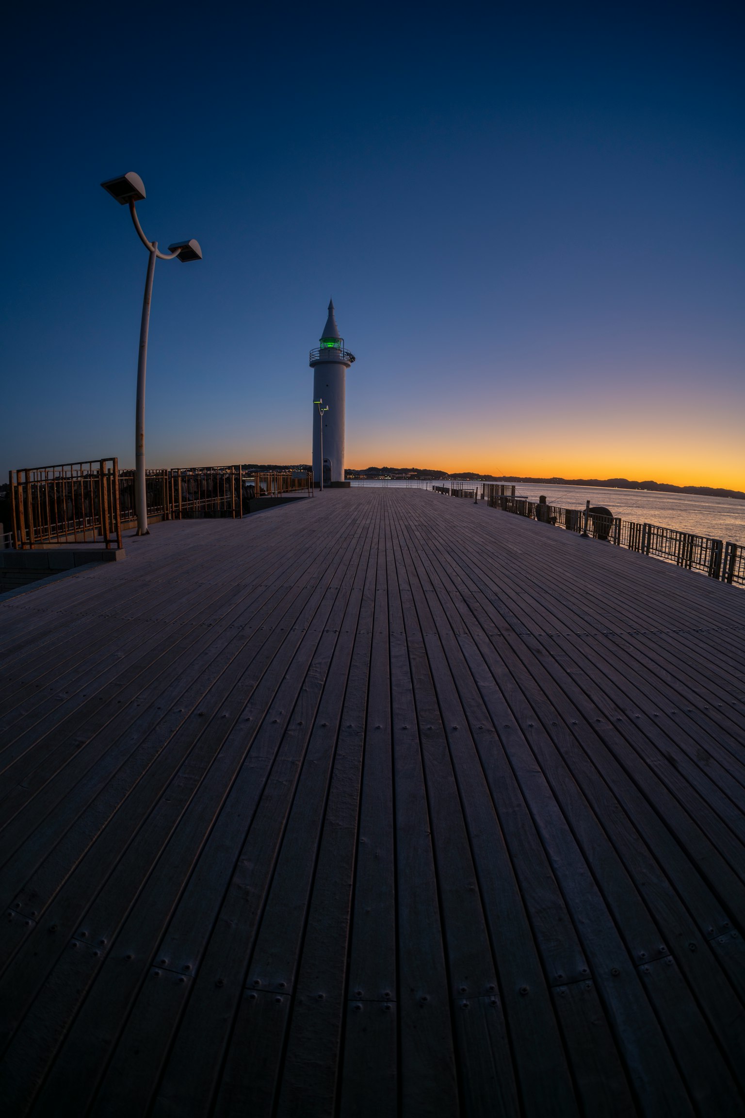 Leuchtturm bei Sonnenuntergang mit einem Holzsteg