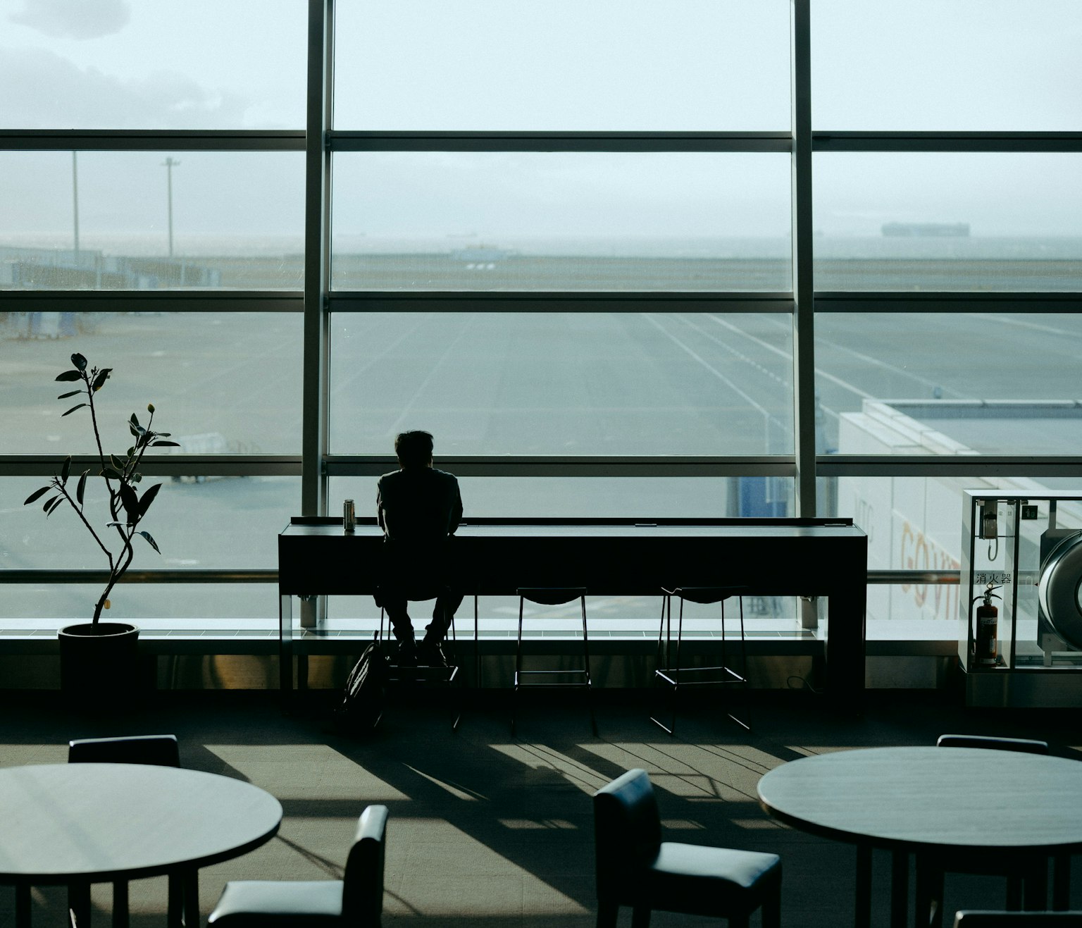 空港のラウンジで窓のそばに座る人影と広がる滑走路の風景