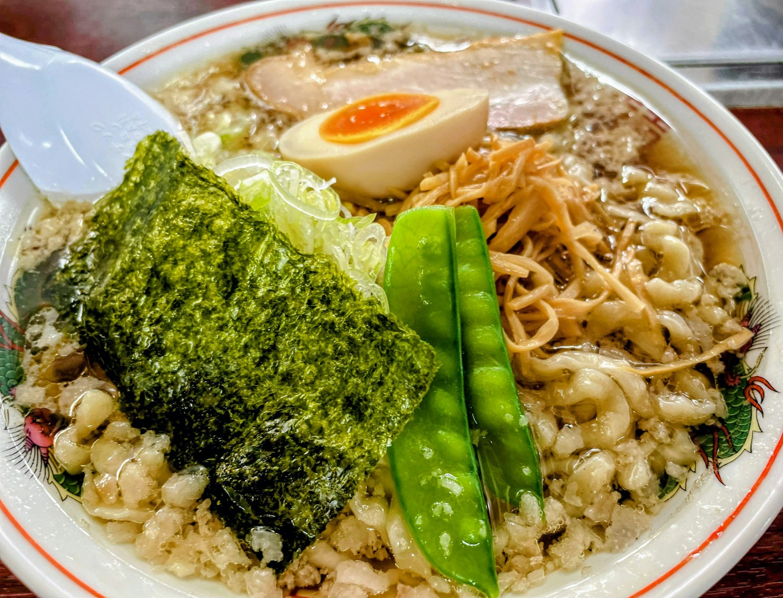 一碗美味的拉面，配有猪肉片、溏心蛋、海苔、青葱、豆芽和豌豆