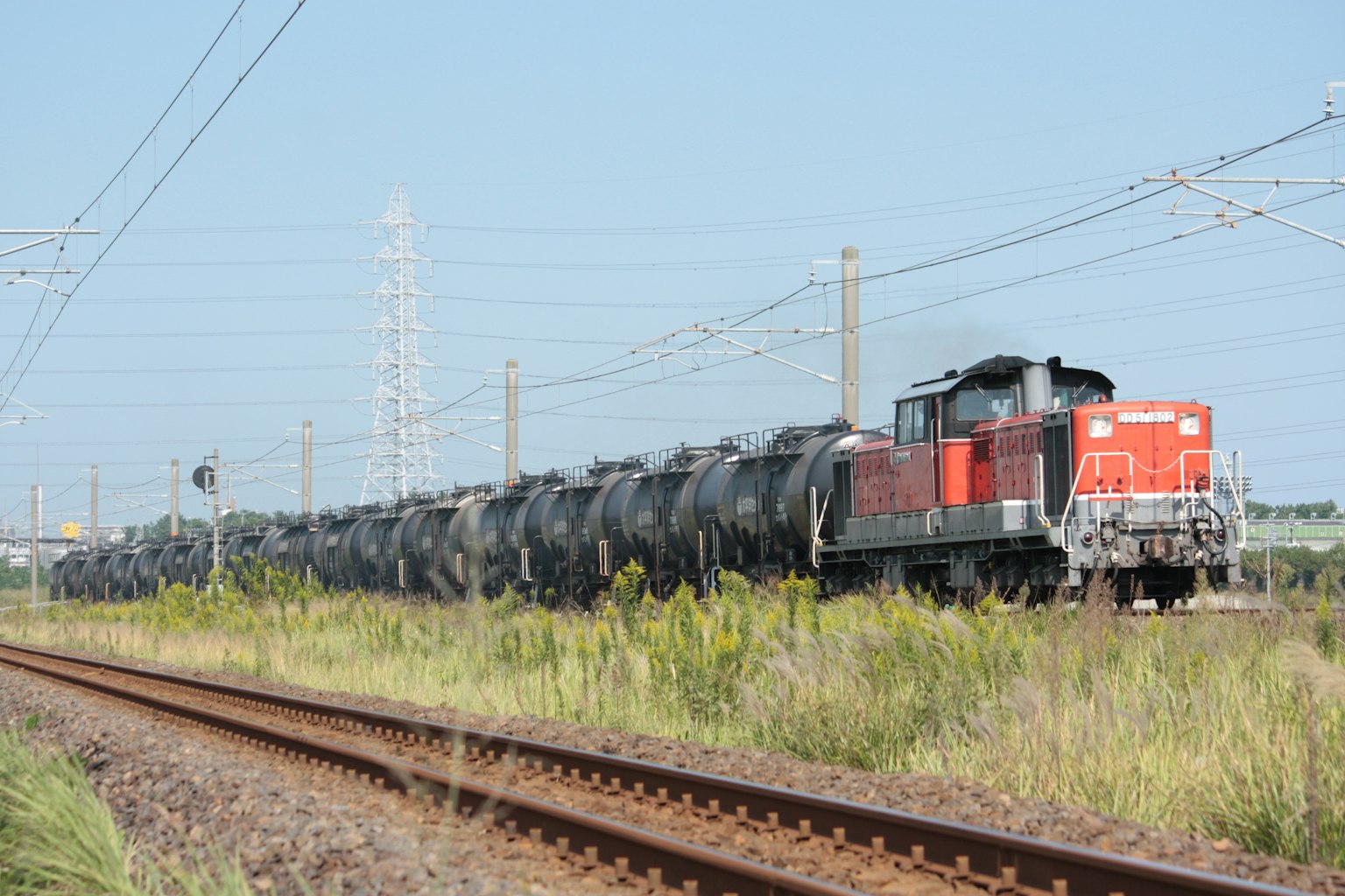 赤いディーゼル機関車が黒いタンク車を牽引する風景