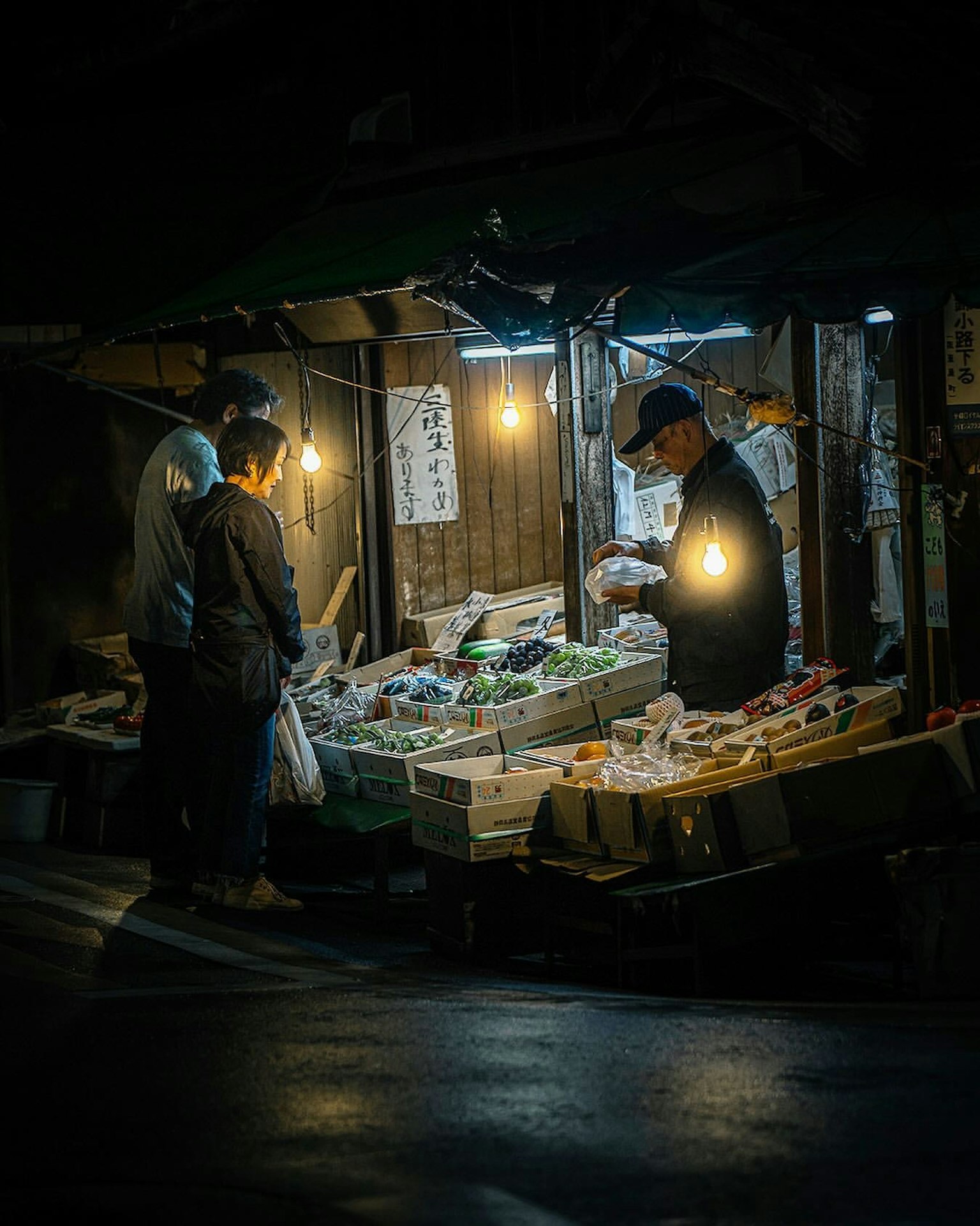 Người chọn rau tại chợ đêm được chiếu sáng bởi ánh đèn ấm áp
