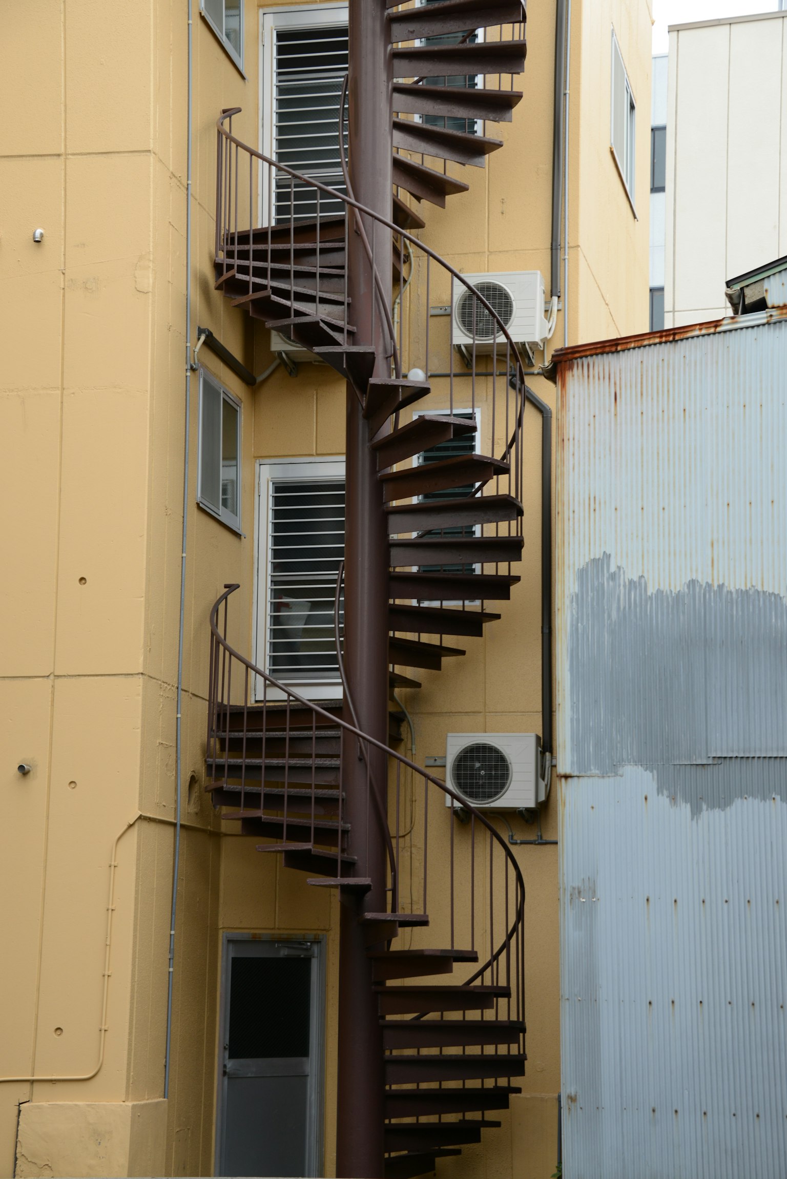 Spiral staircase on the exterior of a yellow building with air conditioning units