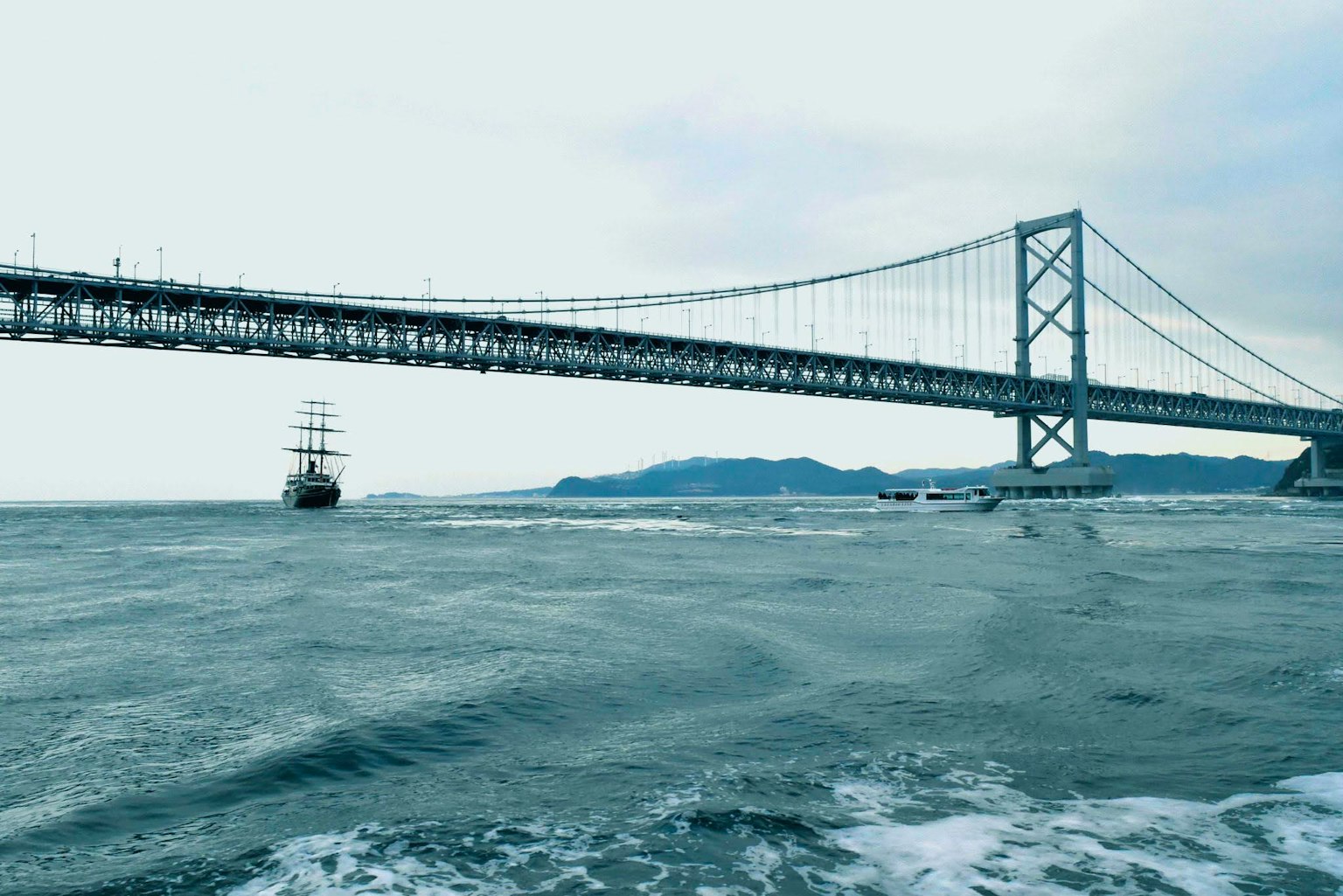 Jembatan besar di atas laut dengan kapal layar terlihat