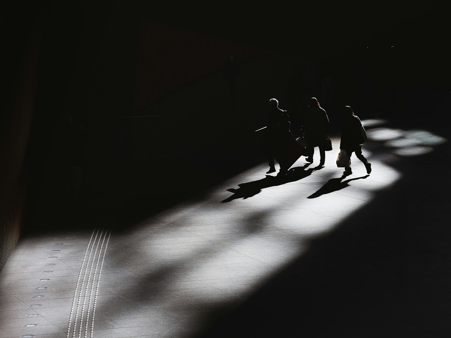 Siluetas de personas caminando en sombras con luz contrastante