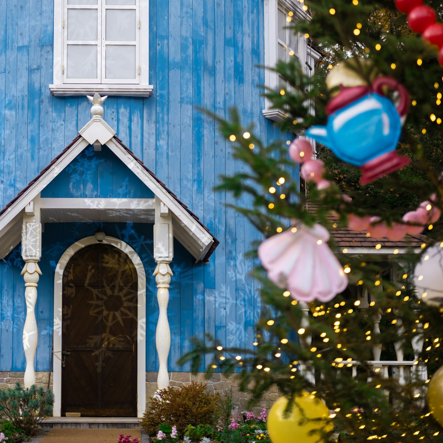 青い外壁の家の入り口とクリスマスツリーの装飾が見える