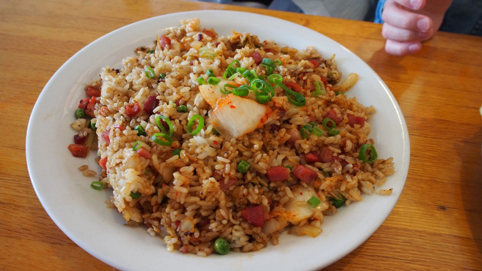 炒饭上面放着青葱和泡菜，盛在白色盘子里