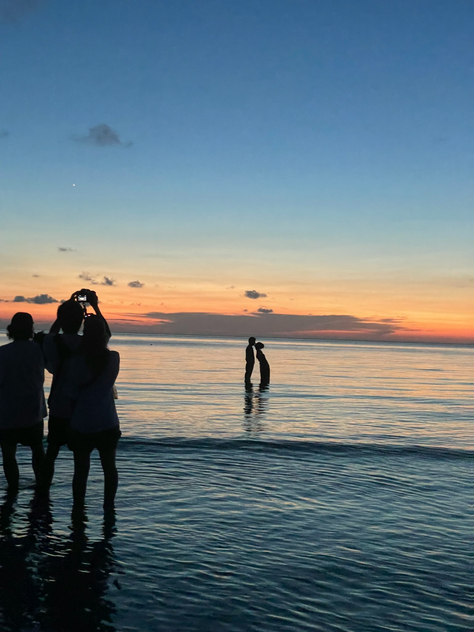 Silhouetten von Menschen, die im Ozean bei Sonnenuntergang stehen