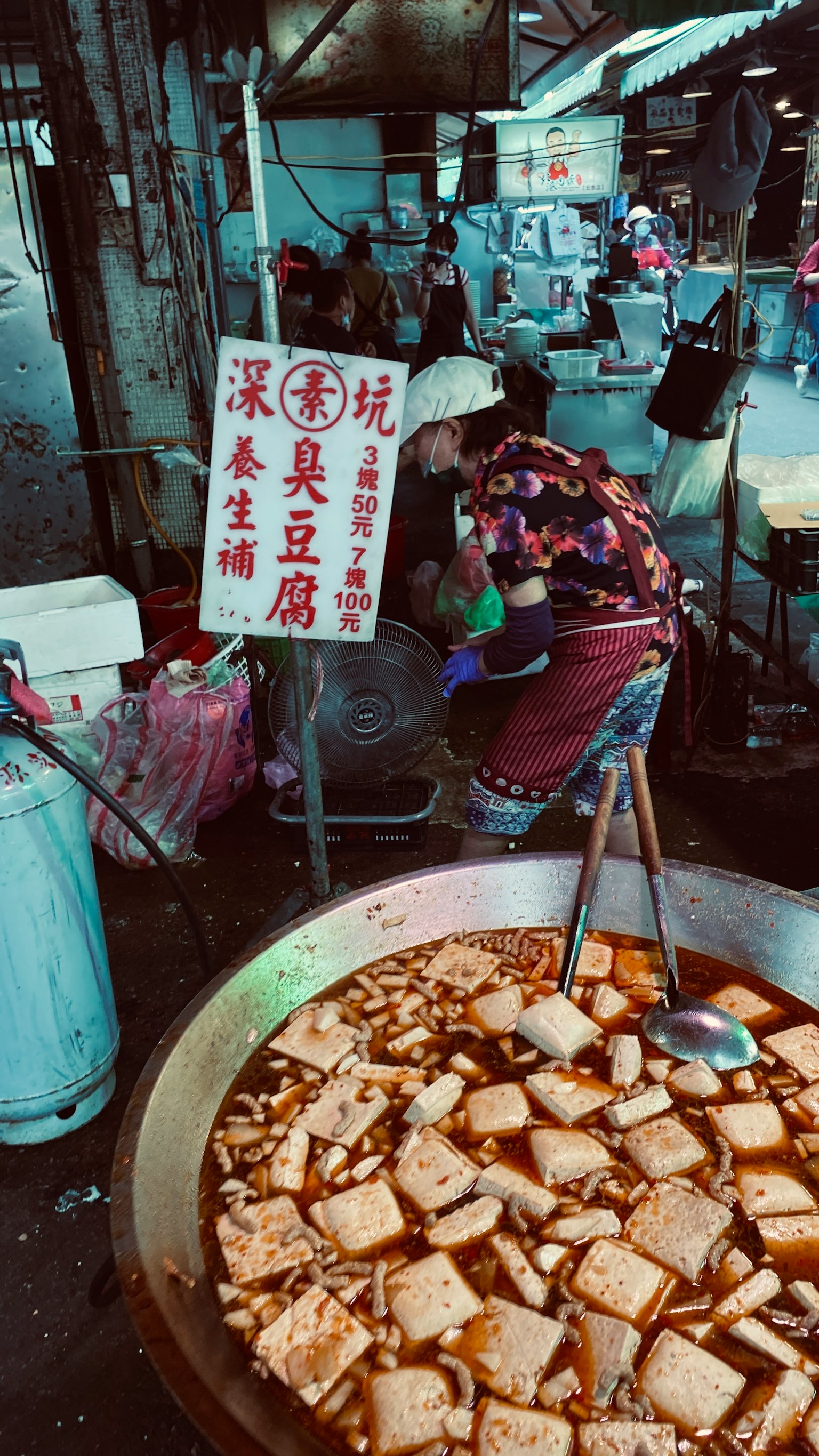 Une femme cuisinant du tofu dans un stand de rue avec un grand pot de tofu