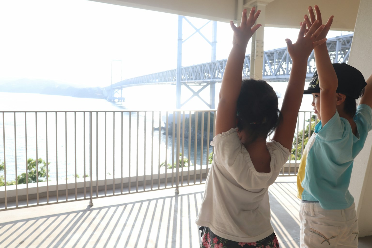 Bambini che alzano le mani con vista su un ponte e il mare