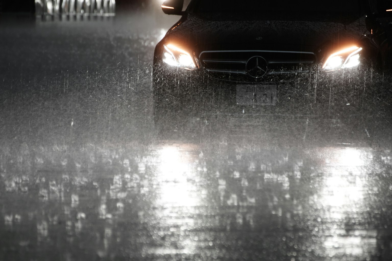 Une voiture Mercedes roulant sous une forte pluie Des phares brillants et des réflexions de gouttes de pluie sont visibles