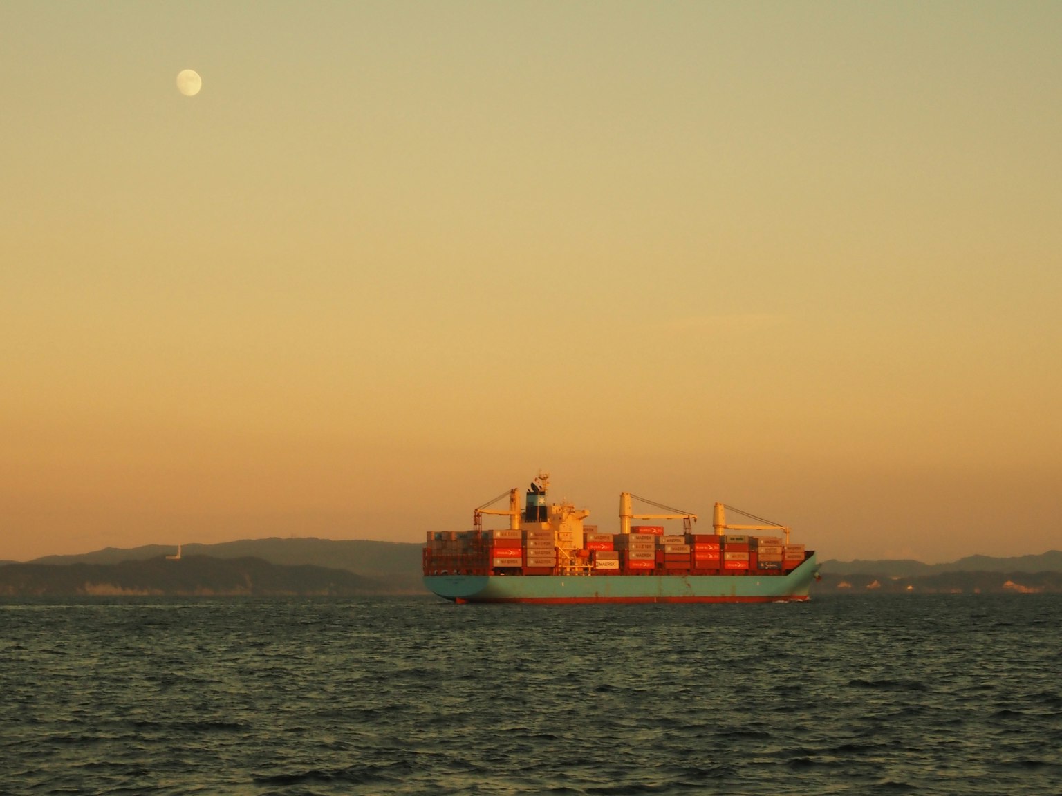 Nave cargo sul mare al tramonto con la luna