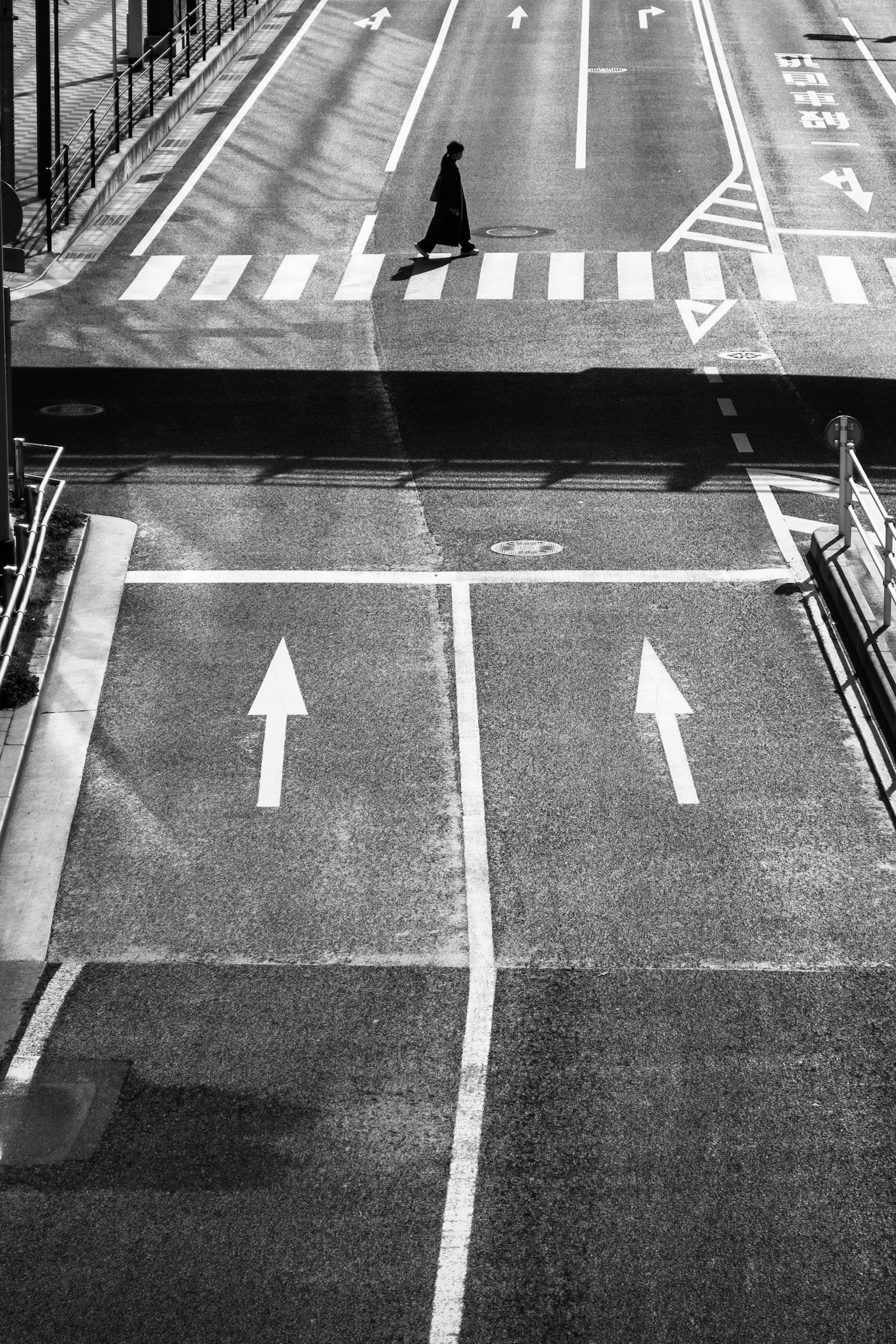 A monochrome street scene showing a person crossing the sidewalk and arrows at an intersection