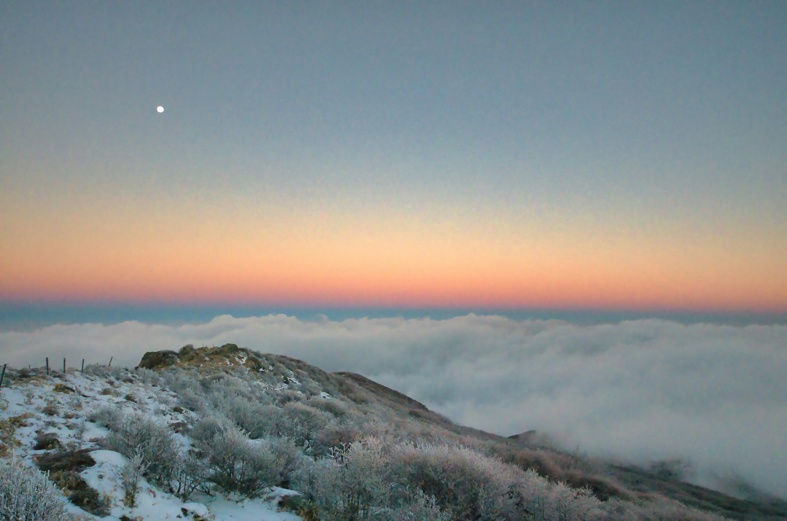Snow-covered mountain peak overlooking a sea of clouds and a sunrise sky