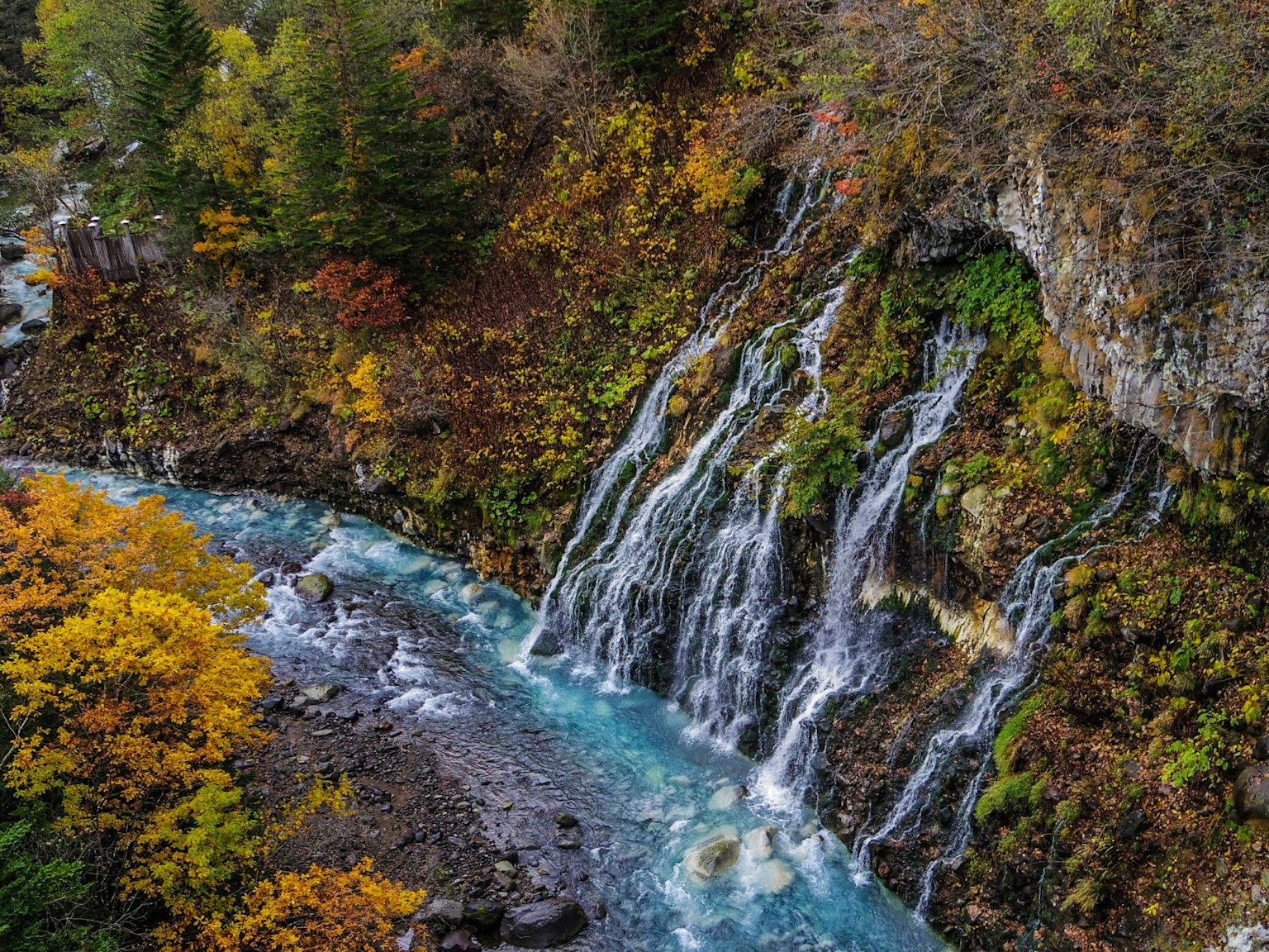 Beautiful waterfall cascading into a blue river surrounded by autumn foliage