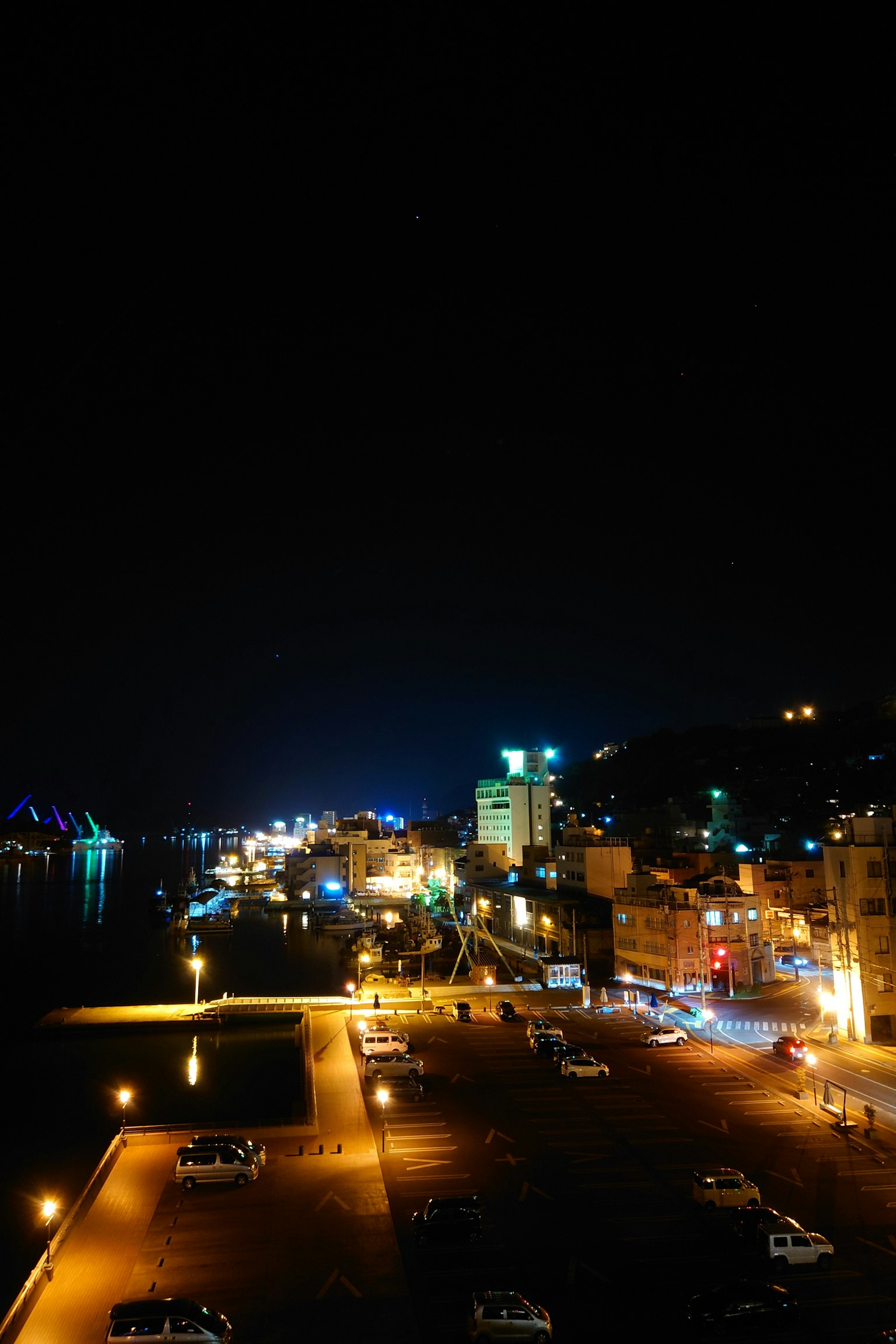 Vista nocturna de un pueblo costero con calles iluminadas y coches estacionados