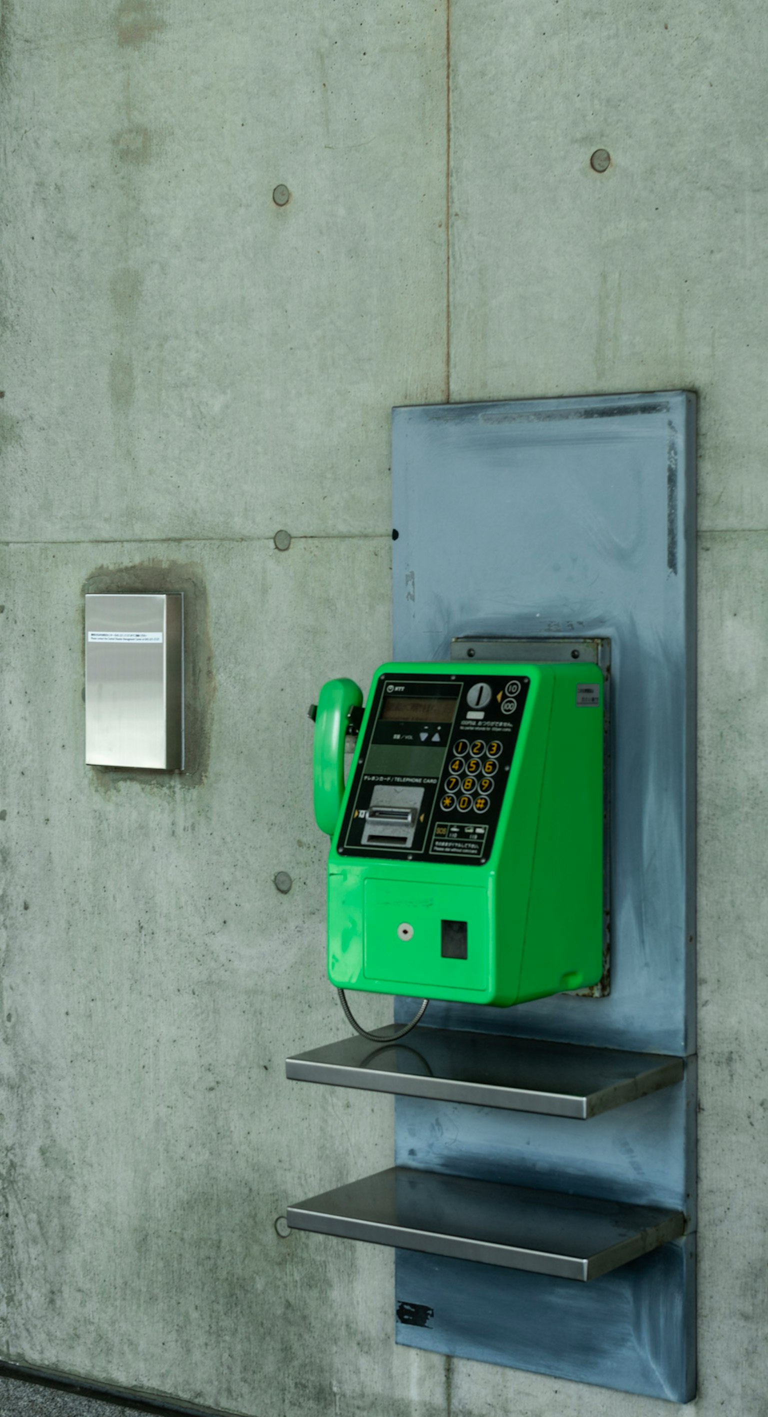 Téléphone public vert monté sur un mur en béton