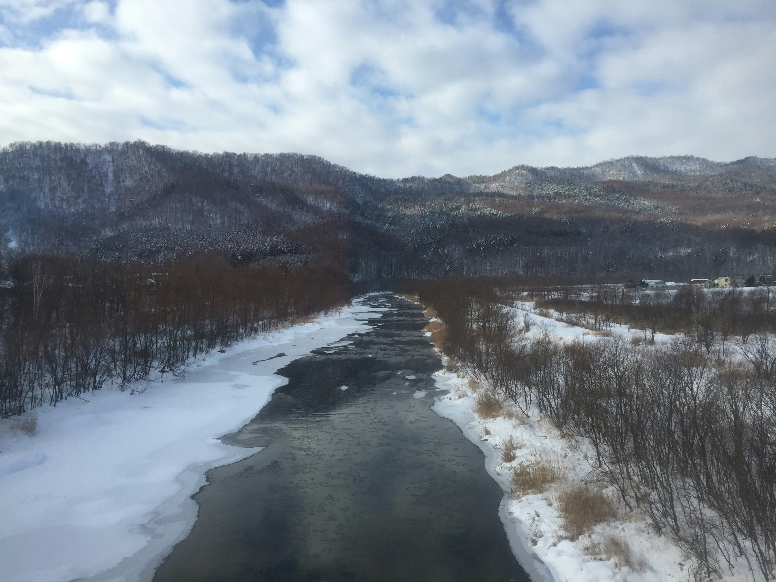 雪原を流れる川と冬の山並みの風景