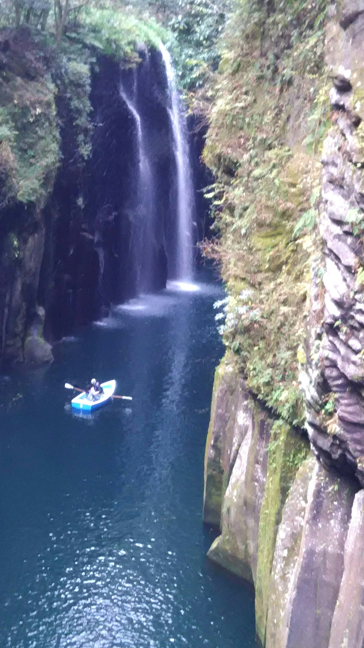 A scenic gorge with a blue kayak drifting near a waterfall