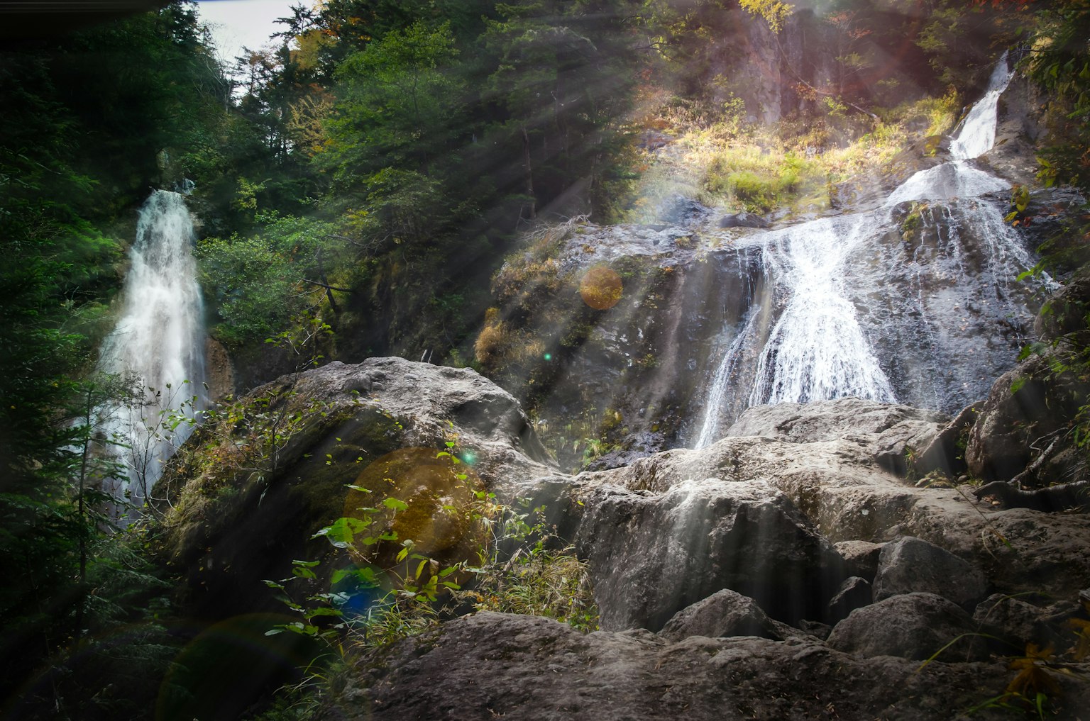 Cascada escénica que cae entre rocas con rayos de sol