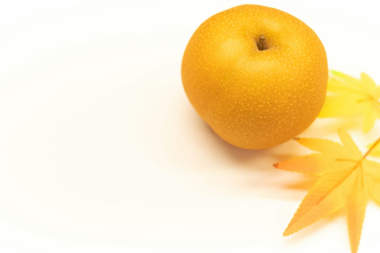 Una fruta amarilla junto a hojas amarillas sobre un fondo blanco