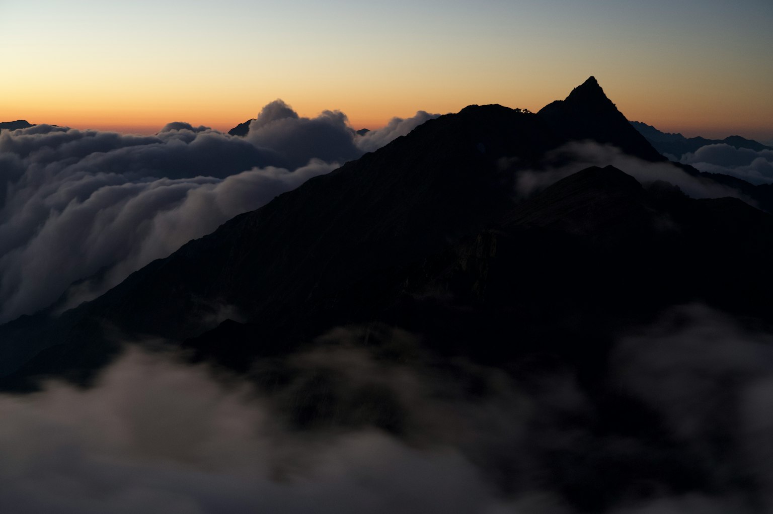 Silhouette of a mountain covered by clouds with a sunset sky